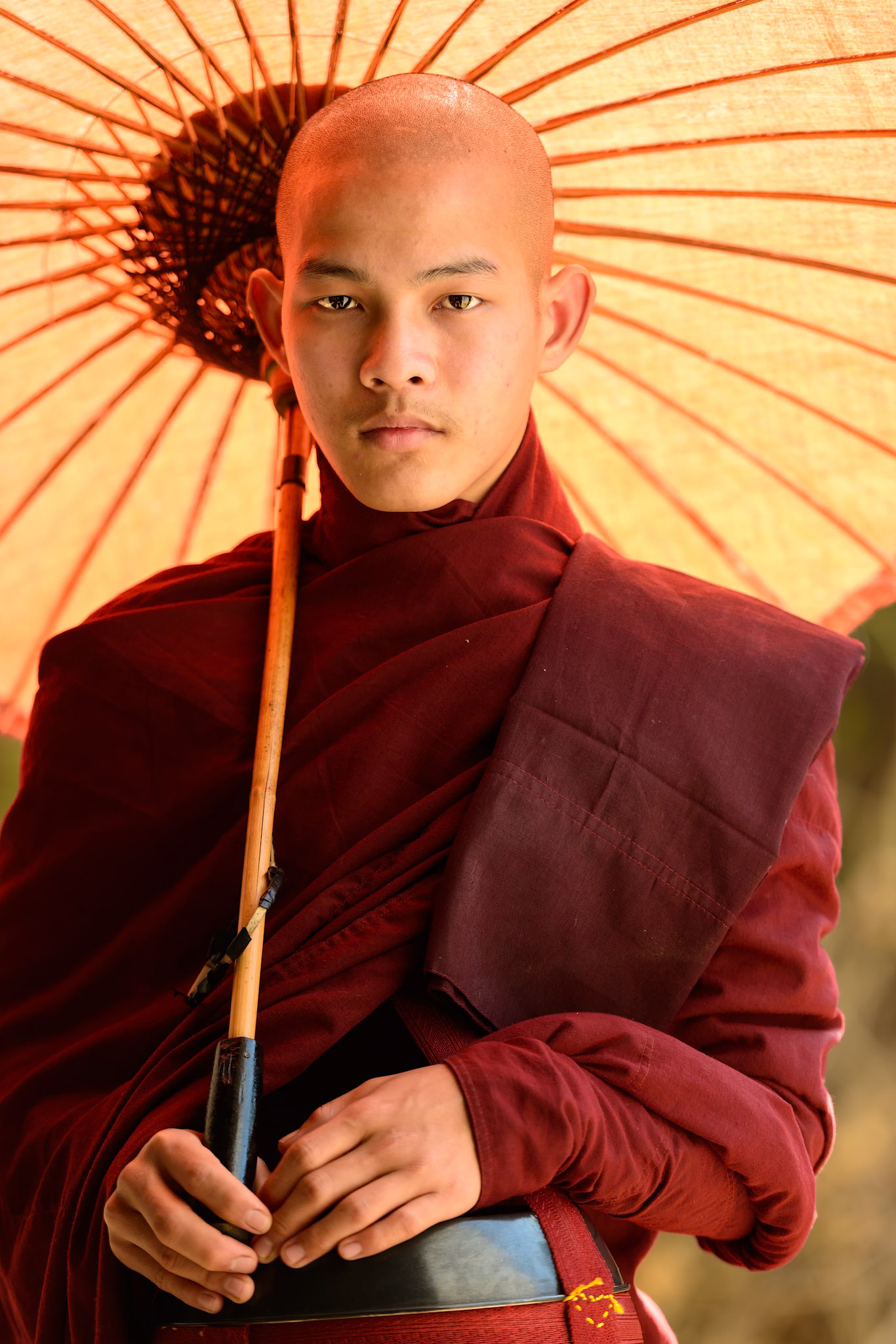 A Bagan monk poses for a photo under a covering of a temple walkway. This was captured in the morning. The monk was positioned by on the edge of the walkway so that the natural light could filter through the parasol and softly illuminate his face. He had a way about him that conveyed a real sense of peace and serenity. This shot was capture in Bagan, Myanmar.
