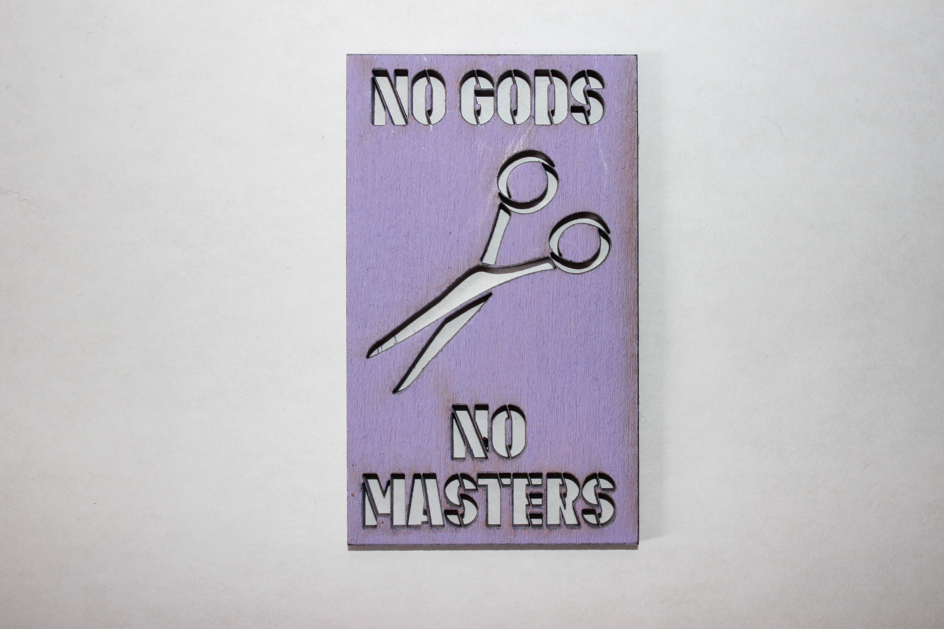 a business card sized wood stencil that says "no gods, no masters" and has a pair of scissors on it