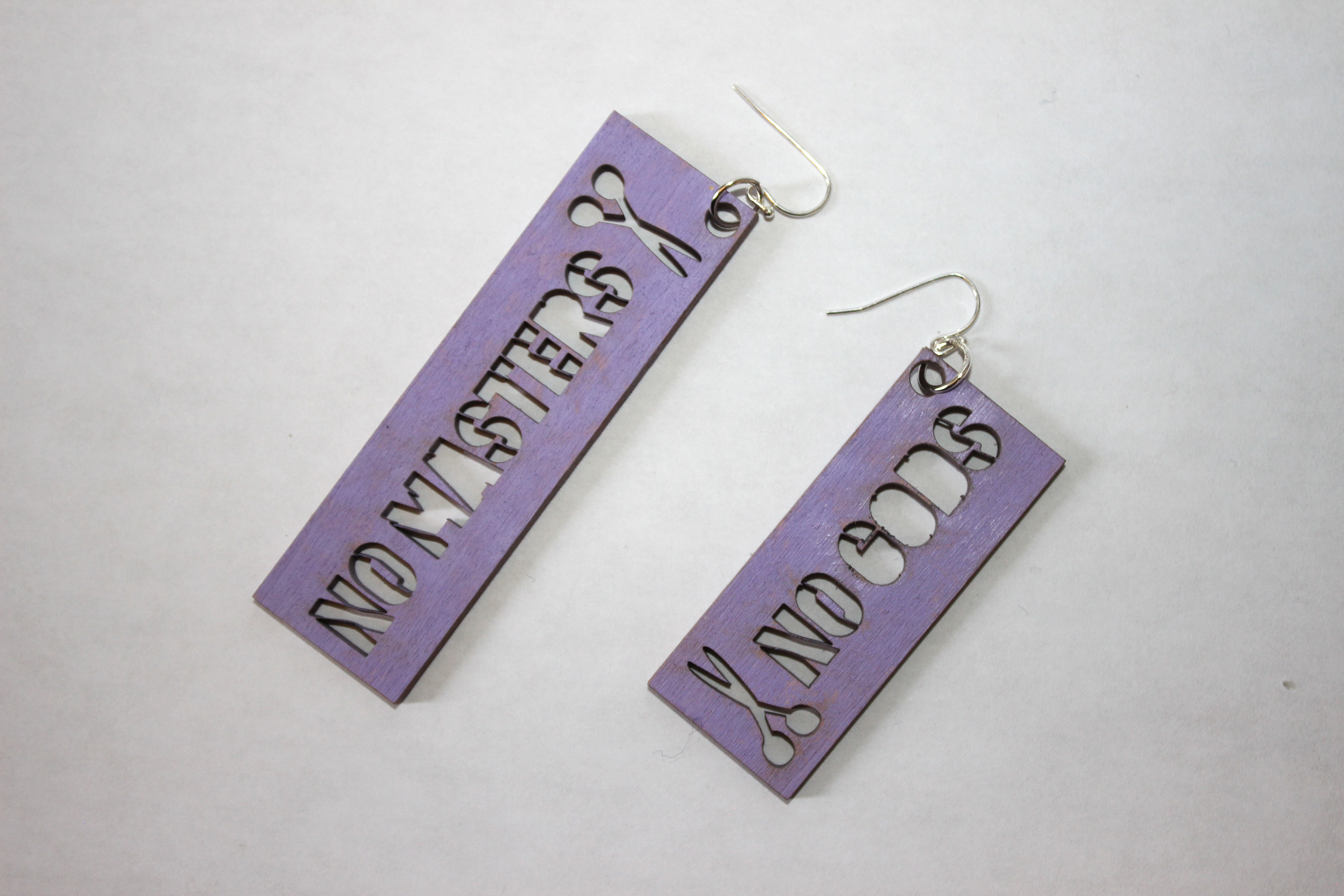 a pair of wood stencil earrings. one says "No gods" with a small pair of scissors. the other says "no masters" with a pair of scissors.