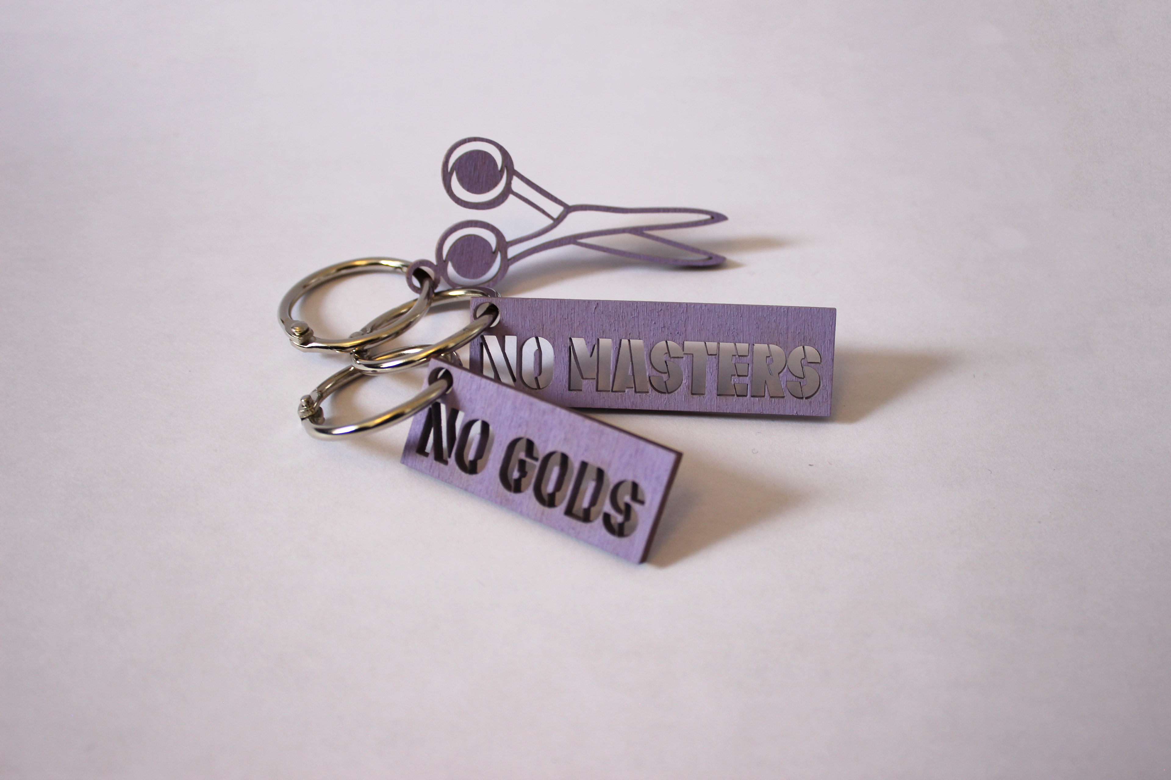 a set of three wood stencil keychains. one says "No Gods", one says "No masters", one is a pair of scissors