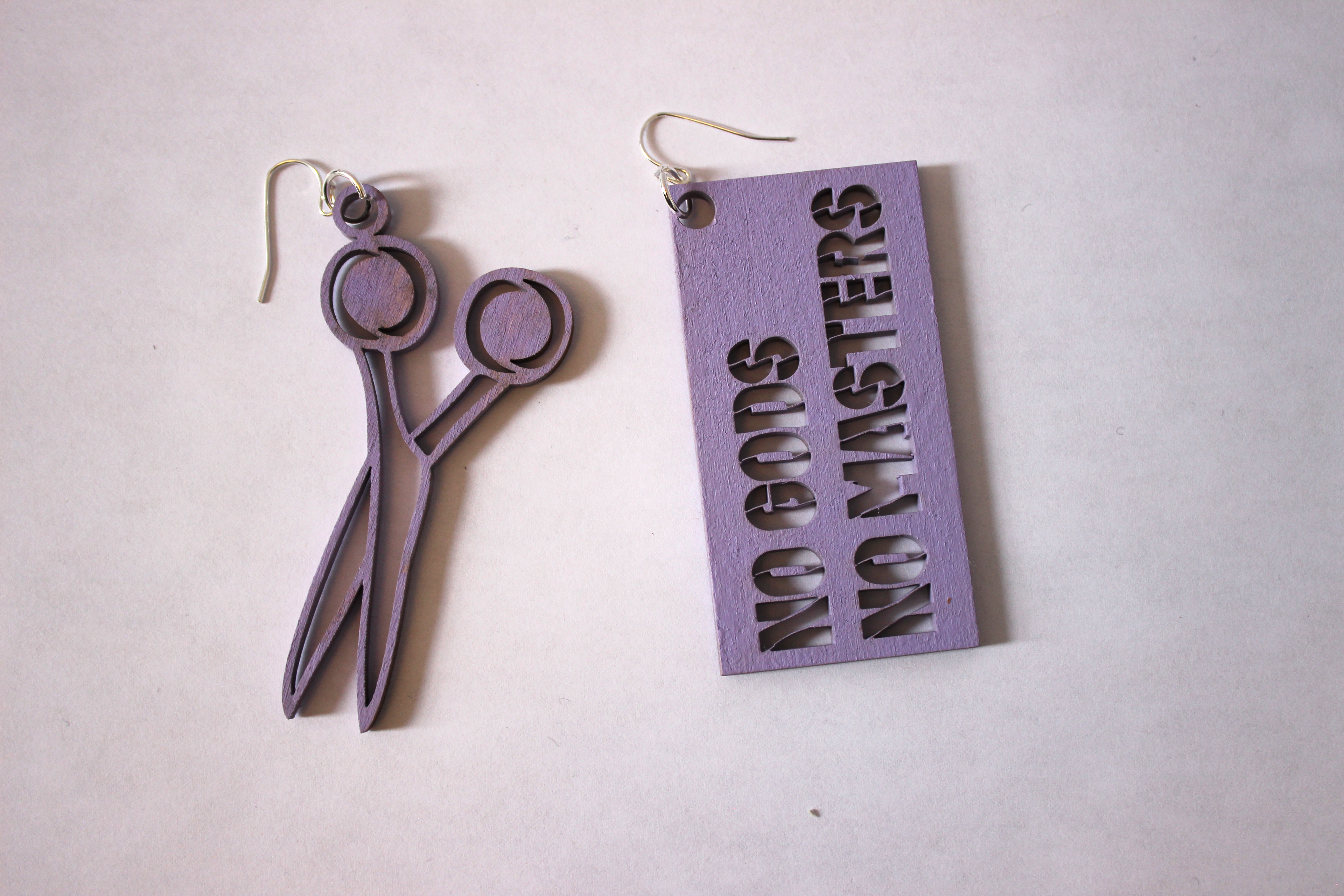 a pair of wood stencil earrings one is a pair of scissors and the other says "No gods, No masters"