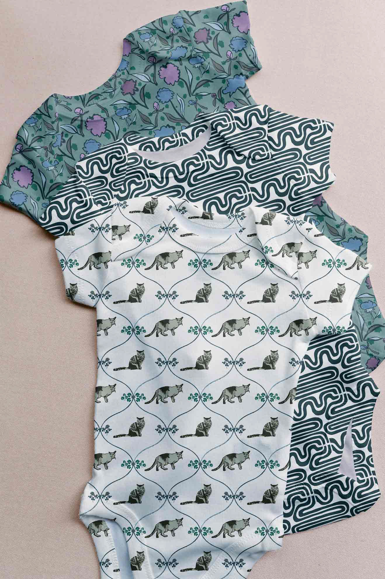 three baby onsies with prints from the crafted colorway. there are cats, squiggle lines, and flowers