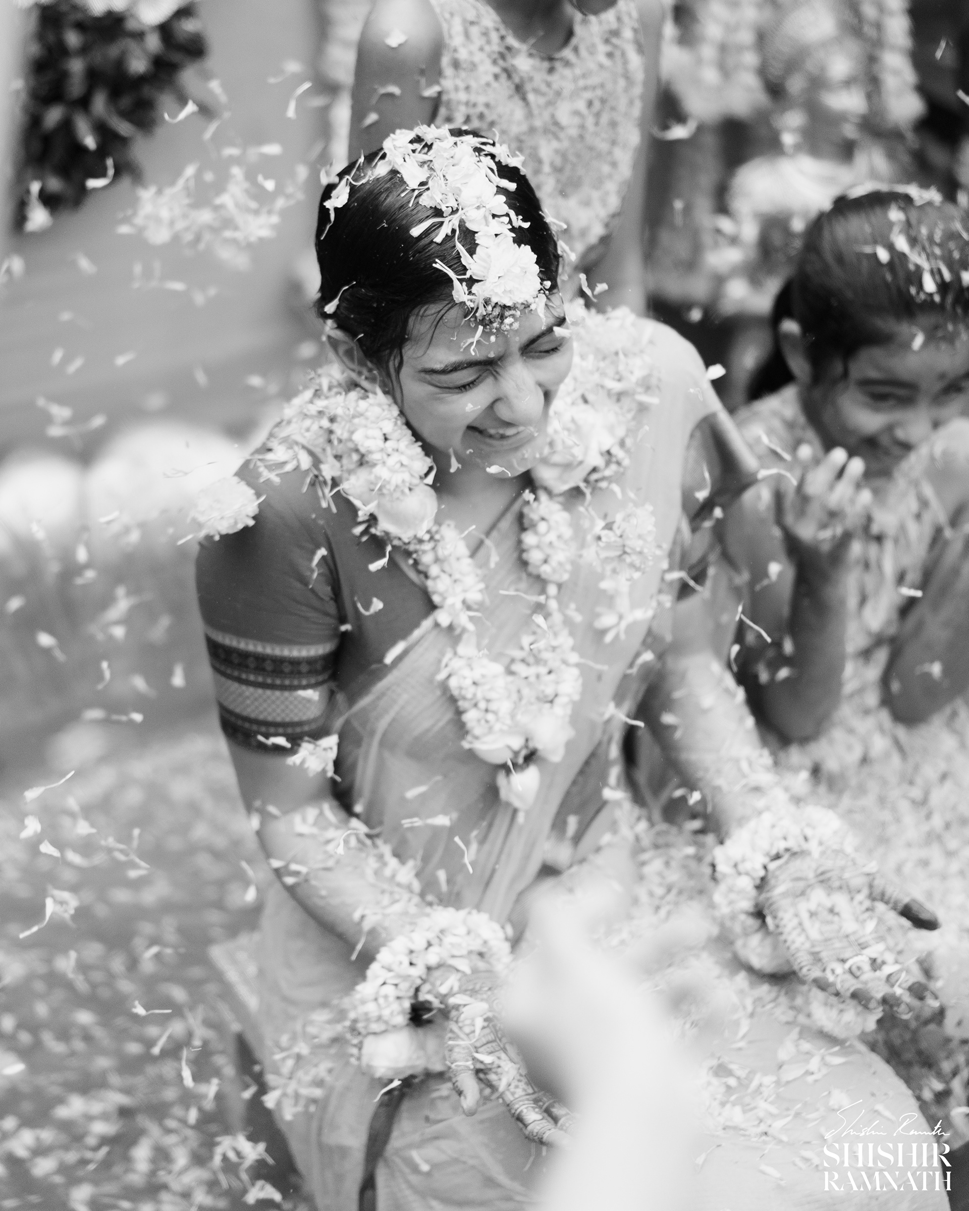 a telugu bride sits amidst flowers being showered on her during a haldi event