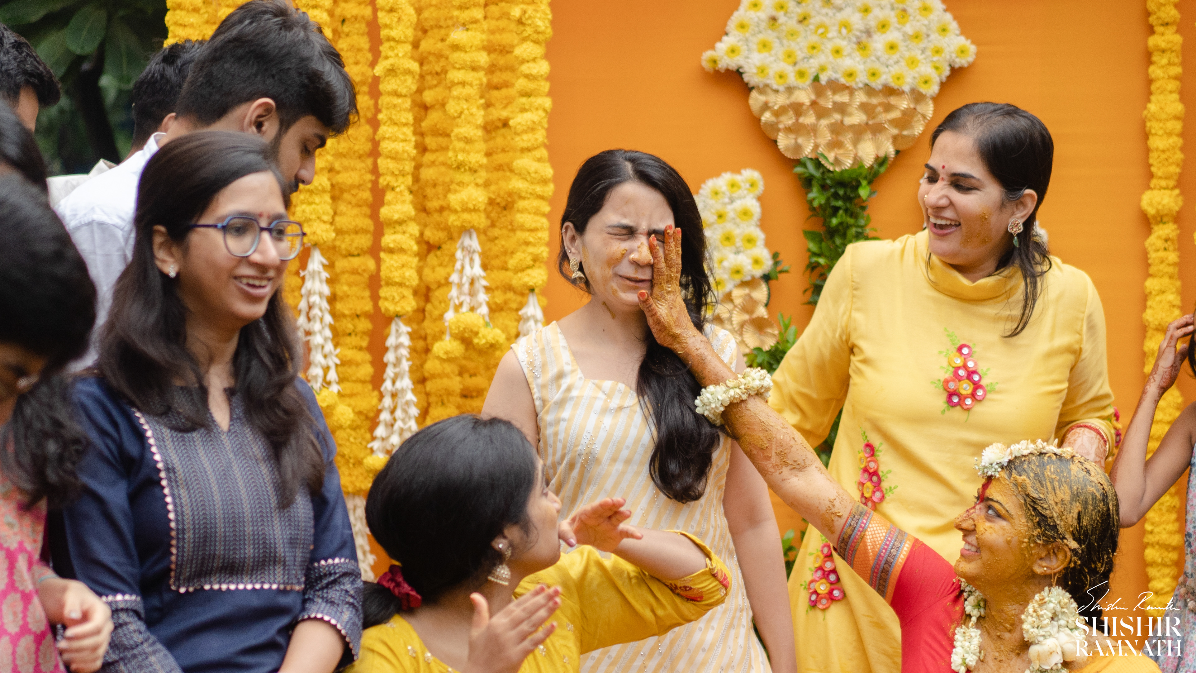 A surprised bridesmaid when she is smeared with haldi on her face at a pre wedding ceremony at home