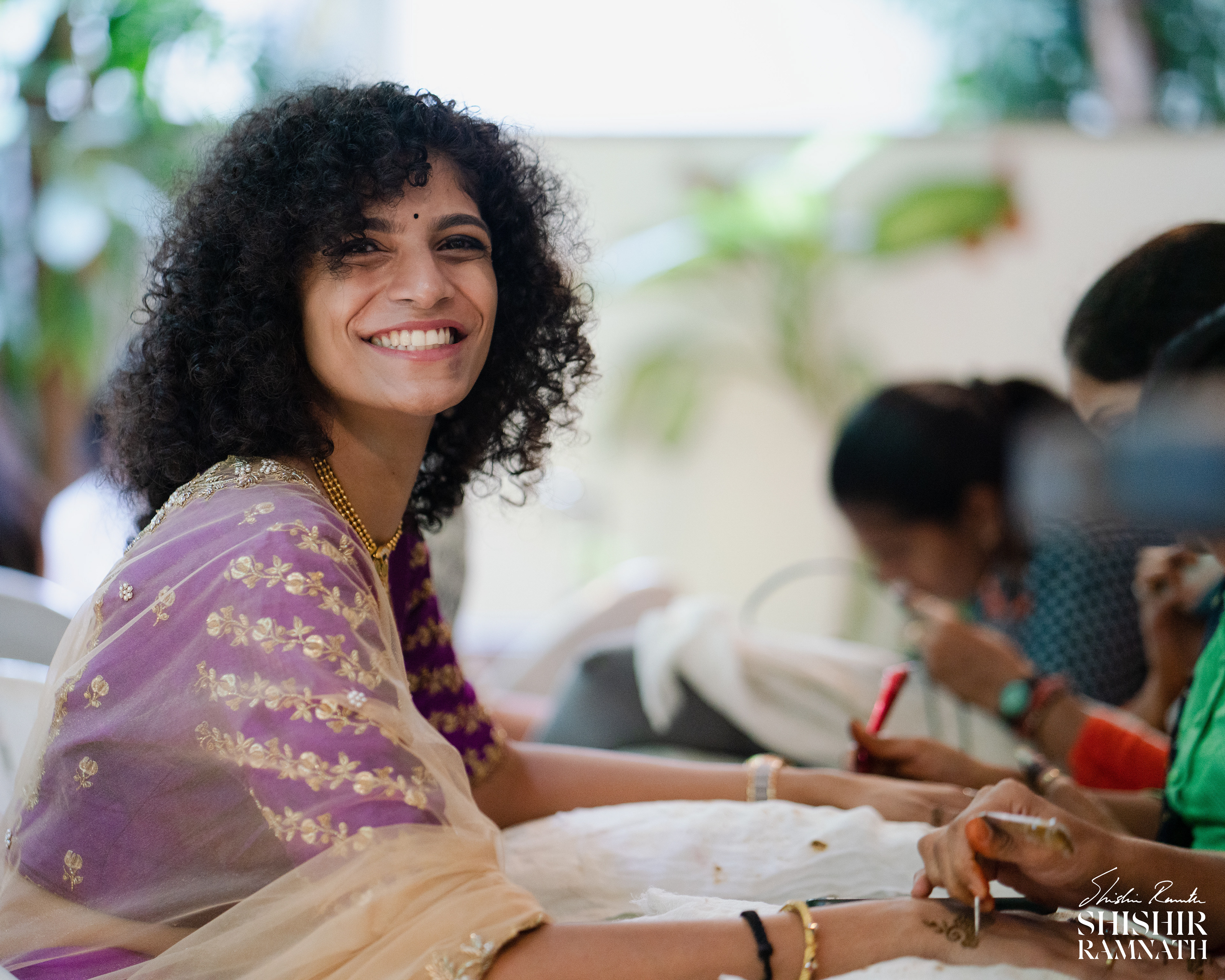 a woman smiling at the camera as shishir ramnath takes a picture