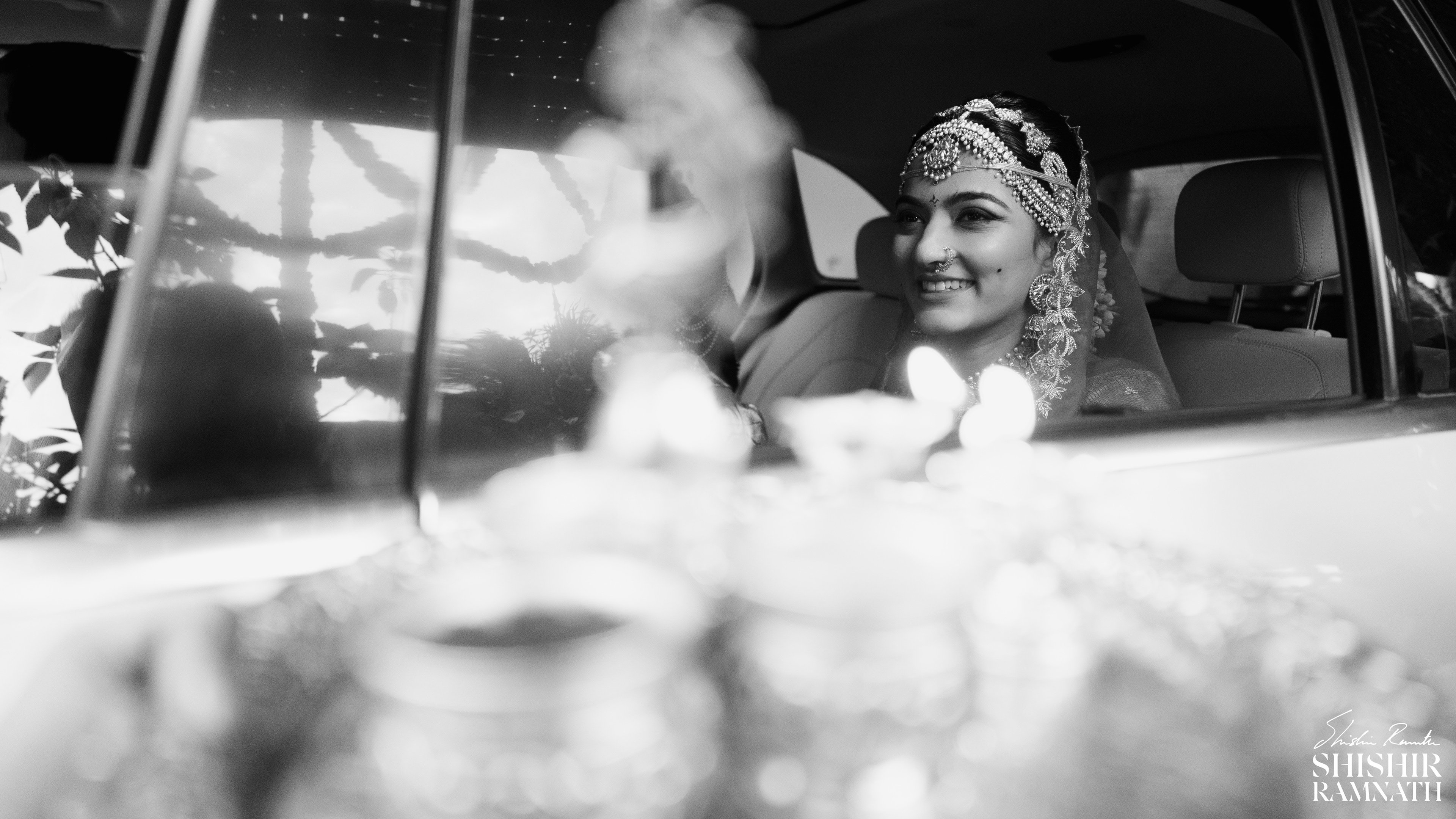 black and white shot of a smiling indian bride leaving to the wedding hall in a car 