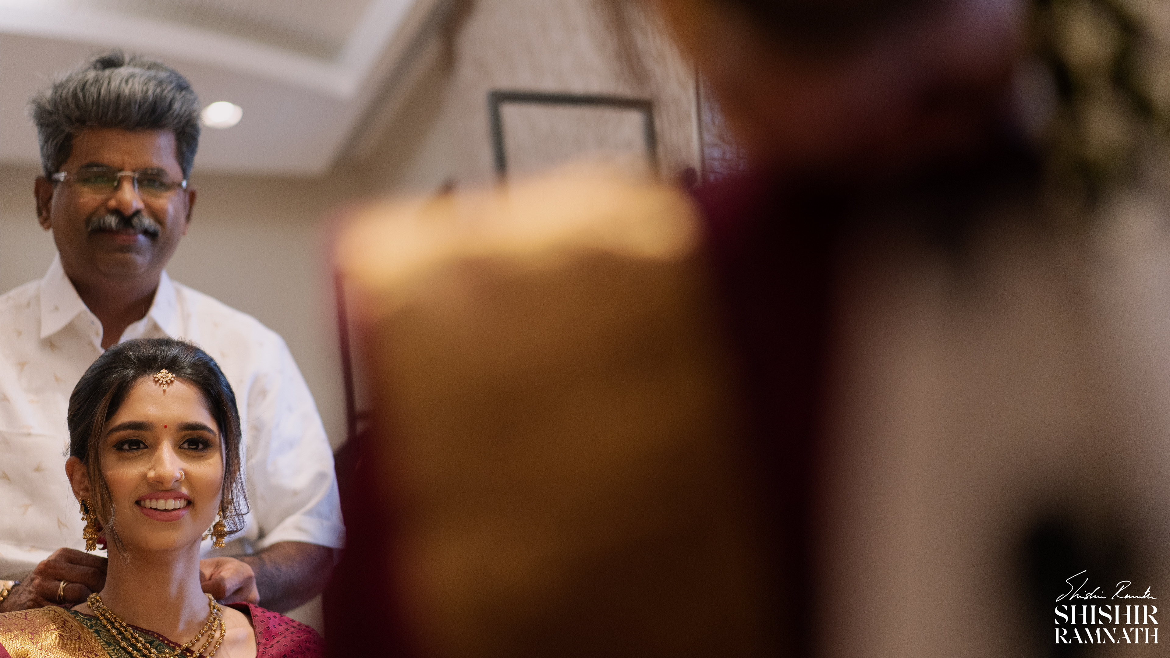 the brides father takes a moment to put on jewelery for his daughter at her wedding they both look into the mirror 