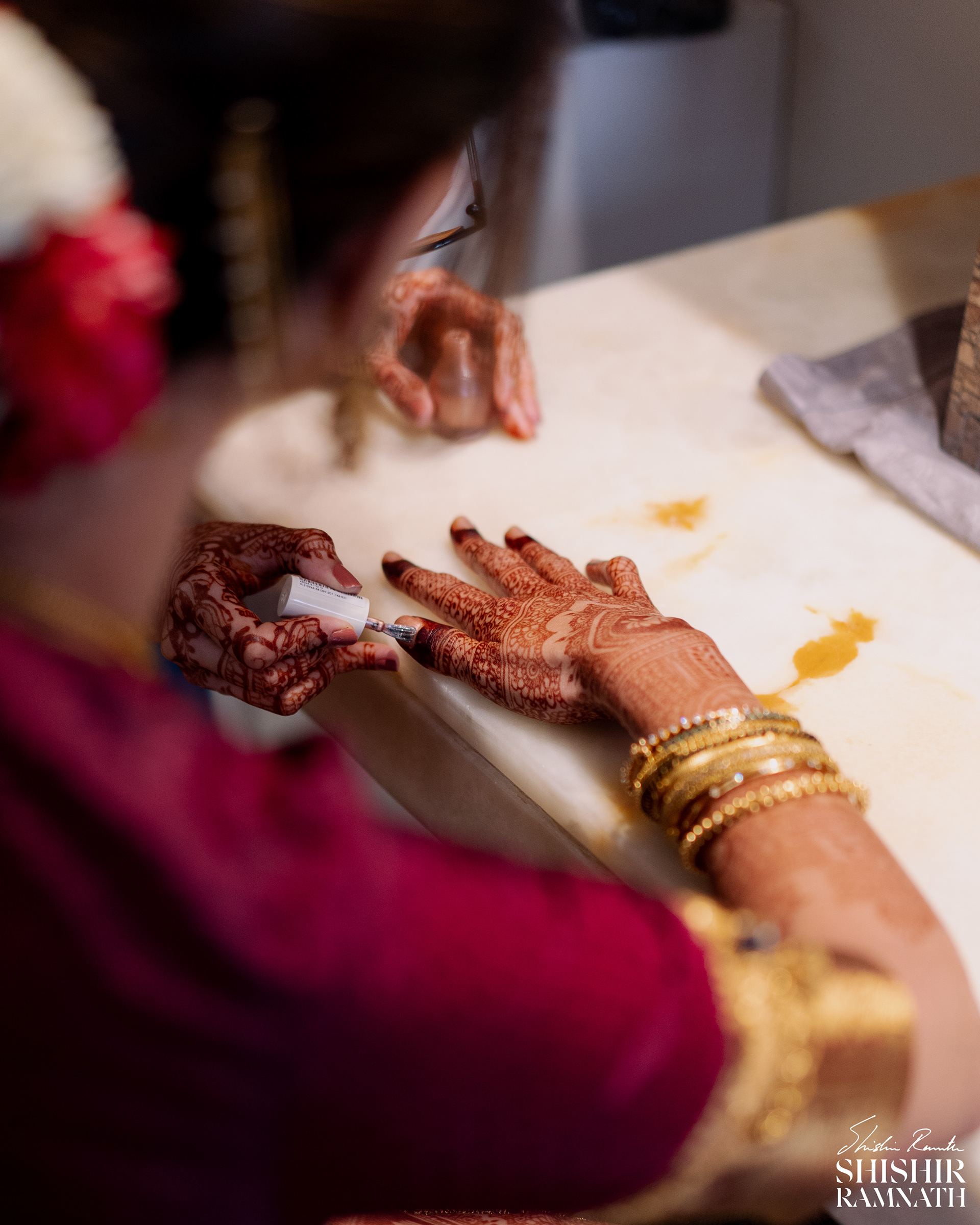 over the shoulder shot of a bride getting her nails painted before her wedding