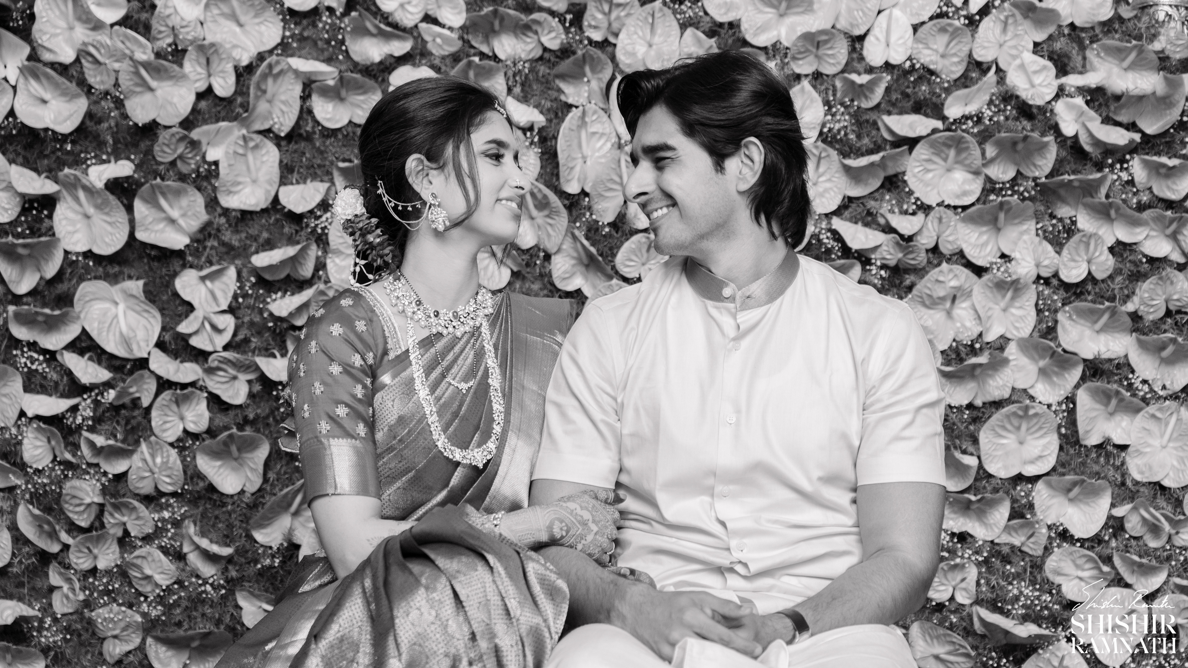 black and white image of a couple look at each other on their wedding day with leaves in the background