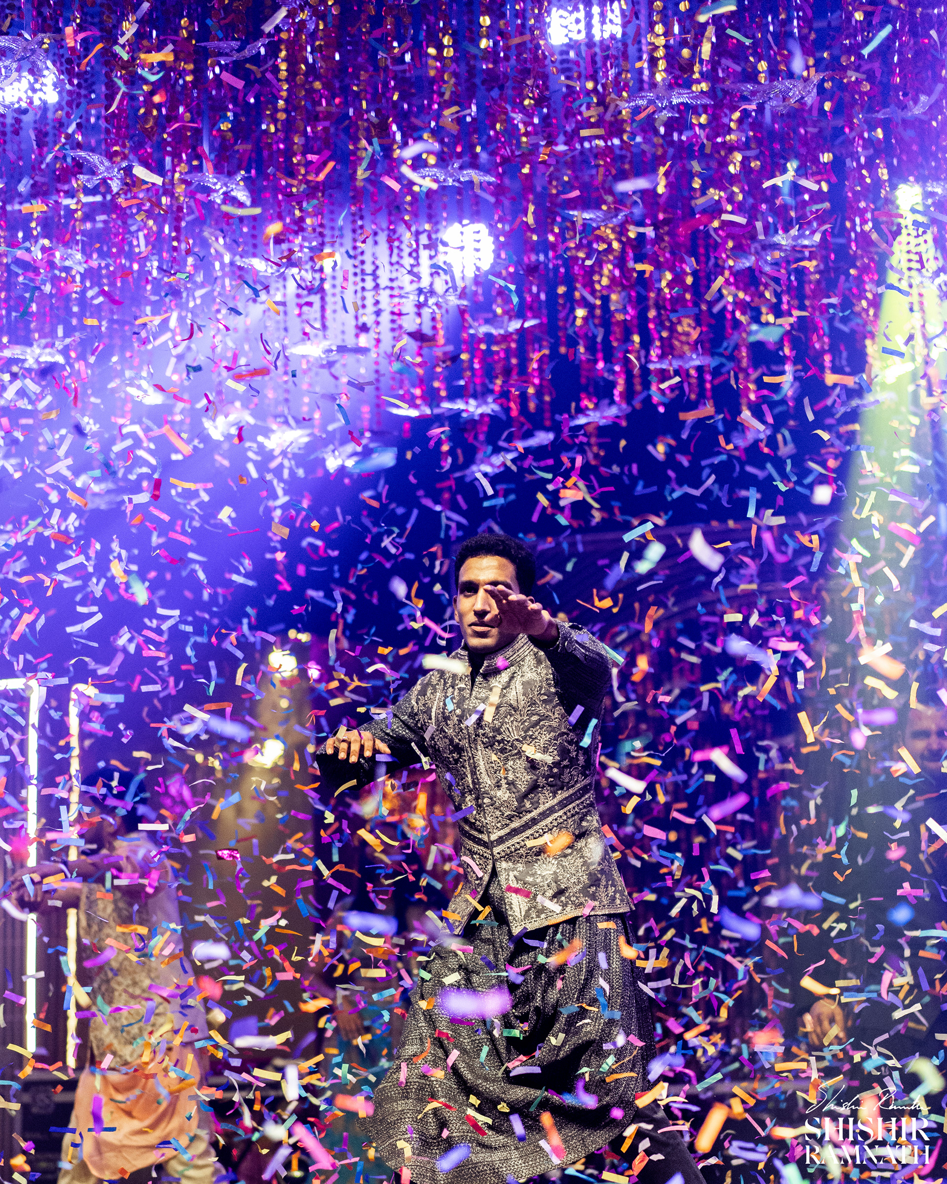 groom showing off his dance moves as party papers fly all around him in a stnning display of energy at an indian wedding
