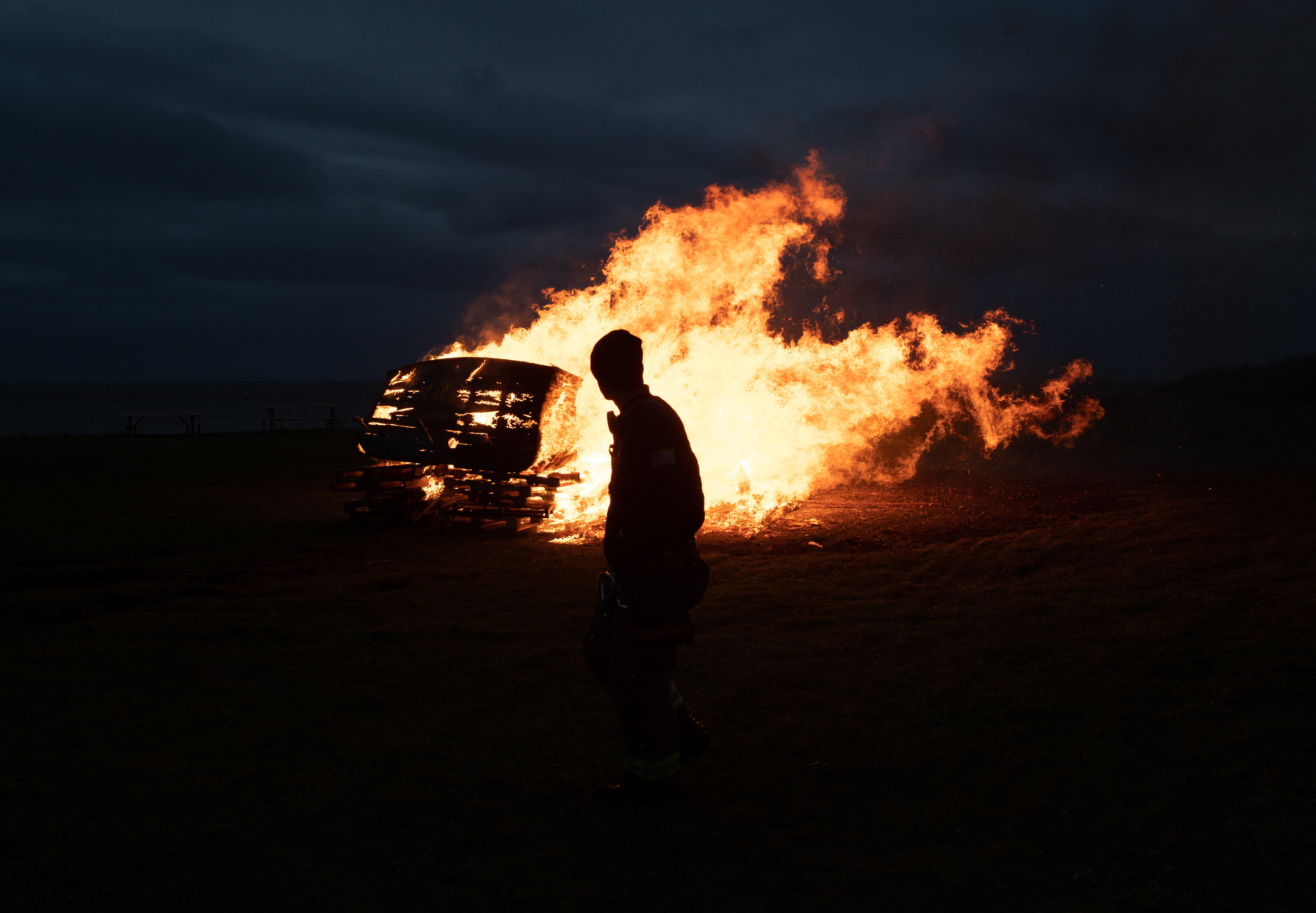 West Sayville Fire Department Volunteer Firefighter Brian Doucet does a routine checkup of a boat fully engulfed in flames during the Long Island Maritime Museum’s 2021 Halloween Boat Burning event. 