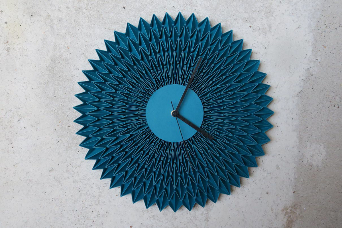Wall clock made of turquoise pleated paper for the set design of a trade fair stand.