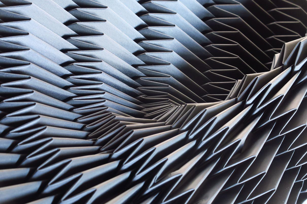 Black synthetic textile manually pleated using folding molds and heat.