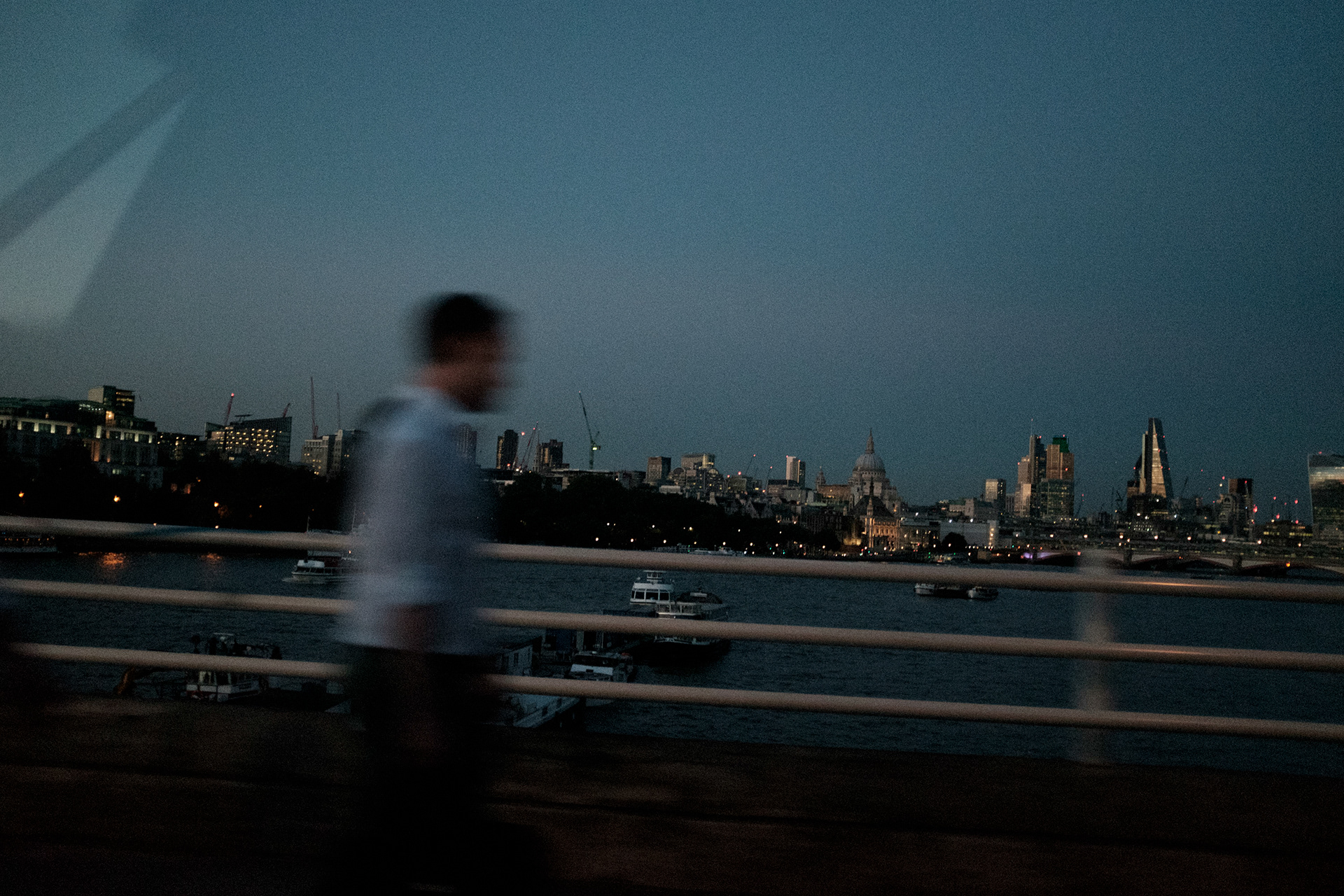 A man is walking on Waterloo Bridge. St Paul's Cathedral and City view behind him. London City Photography. Evren Akozbek.