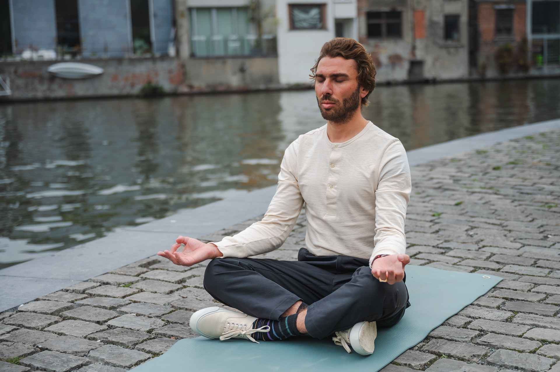 Man meditating cross-legged on a yoga mat by the water in Ghent
