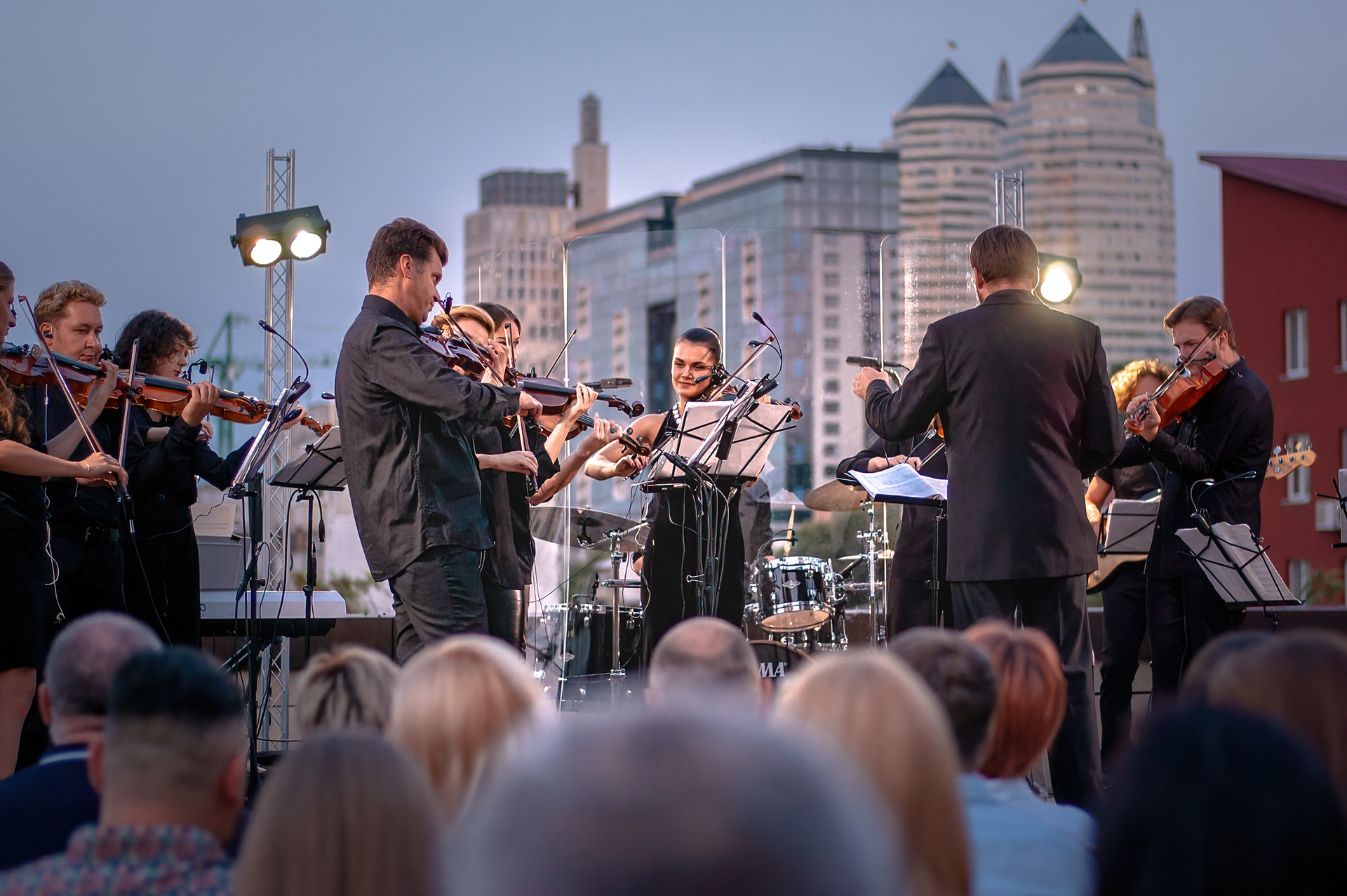 String orchestra and conductor at a rooftop concert, city towers behind them