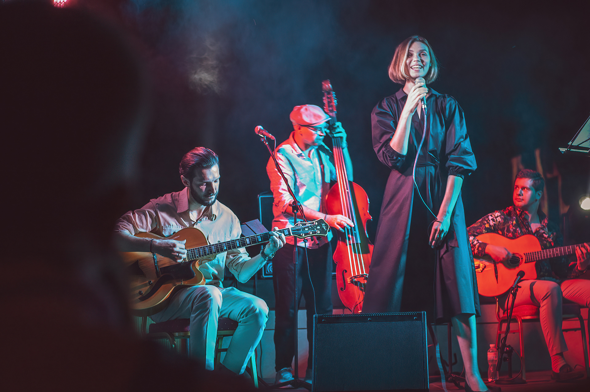 Smiling jazz singer with two guitarists and a double bass player on a smoky stage