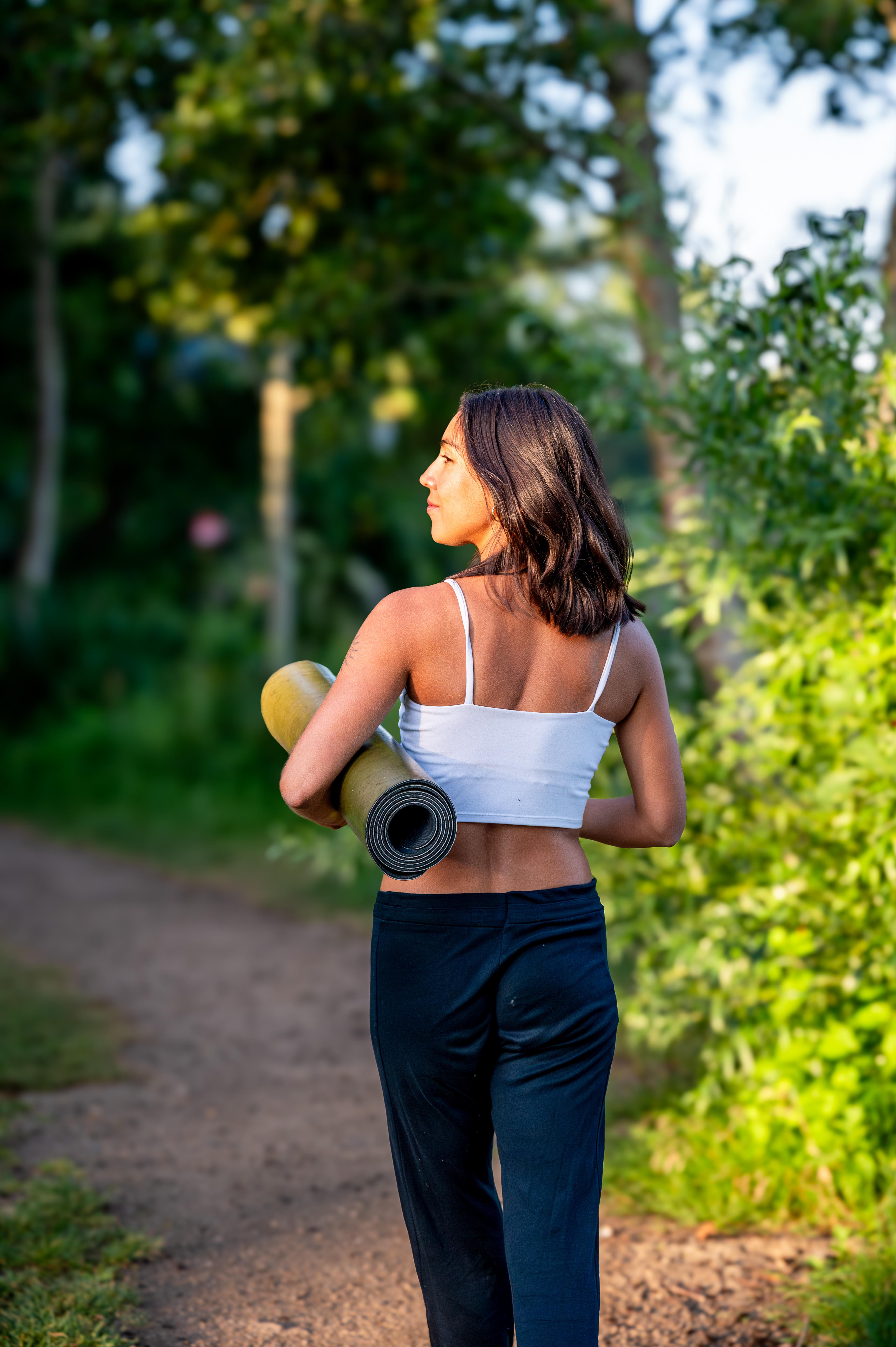 Yoga teacher walking along a forest path with her mat