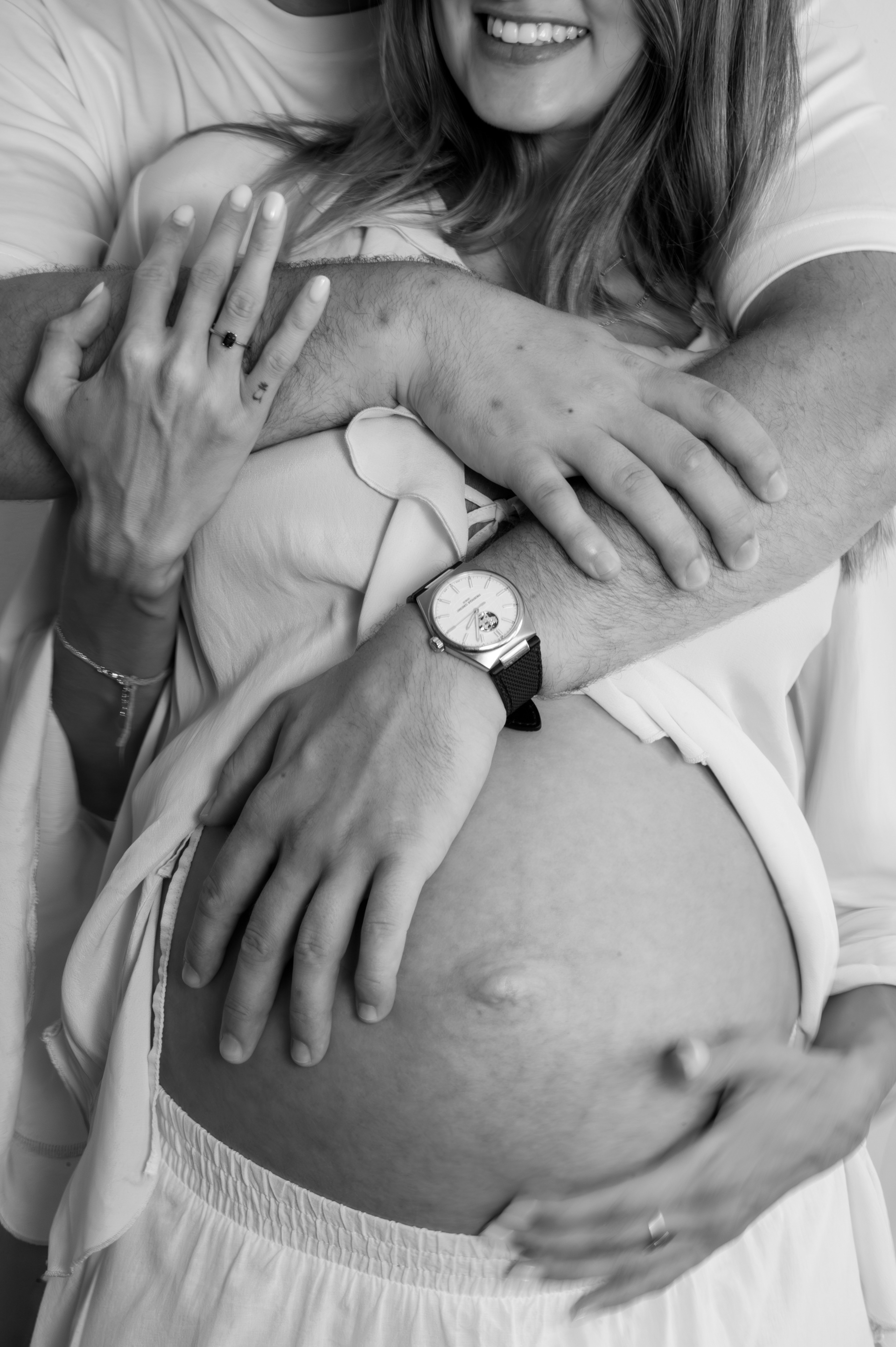 Partner's arms hugging a pregnant woman from behind, black and white