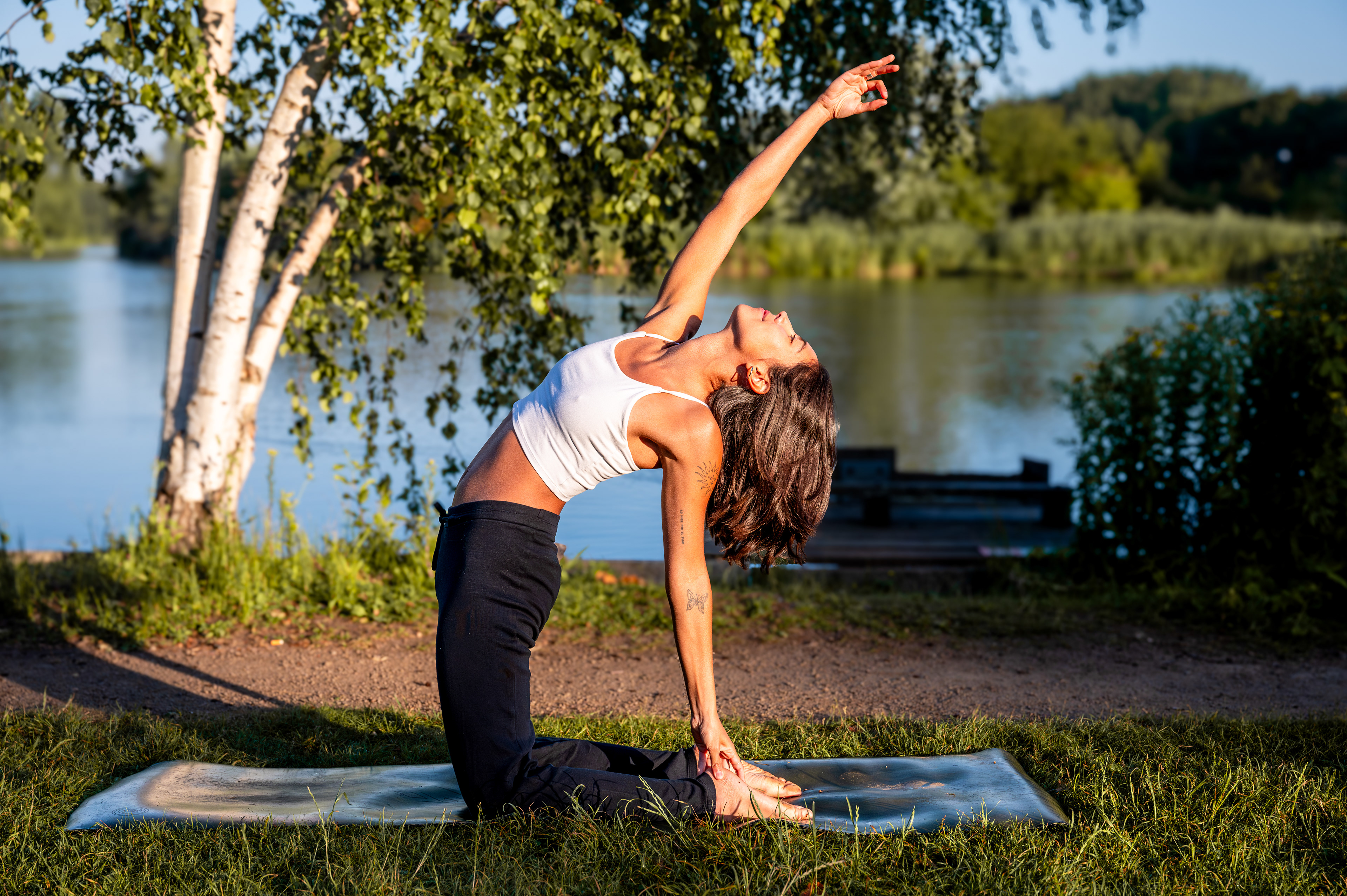 Camel pose on a yoga mat by the lake in evening sun