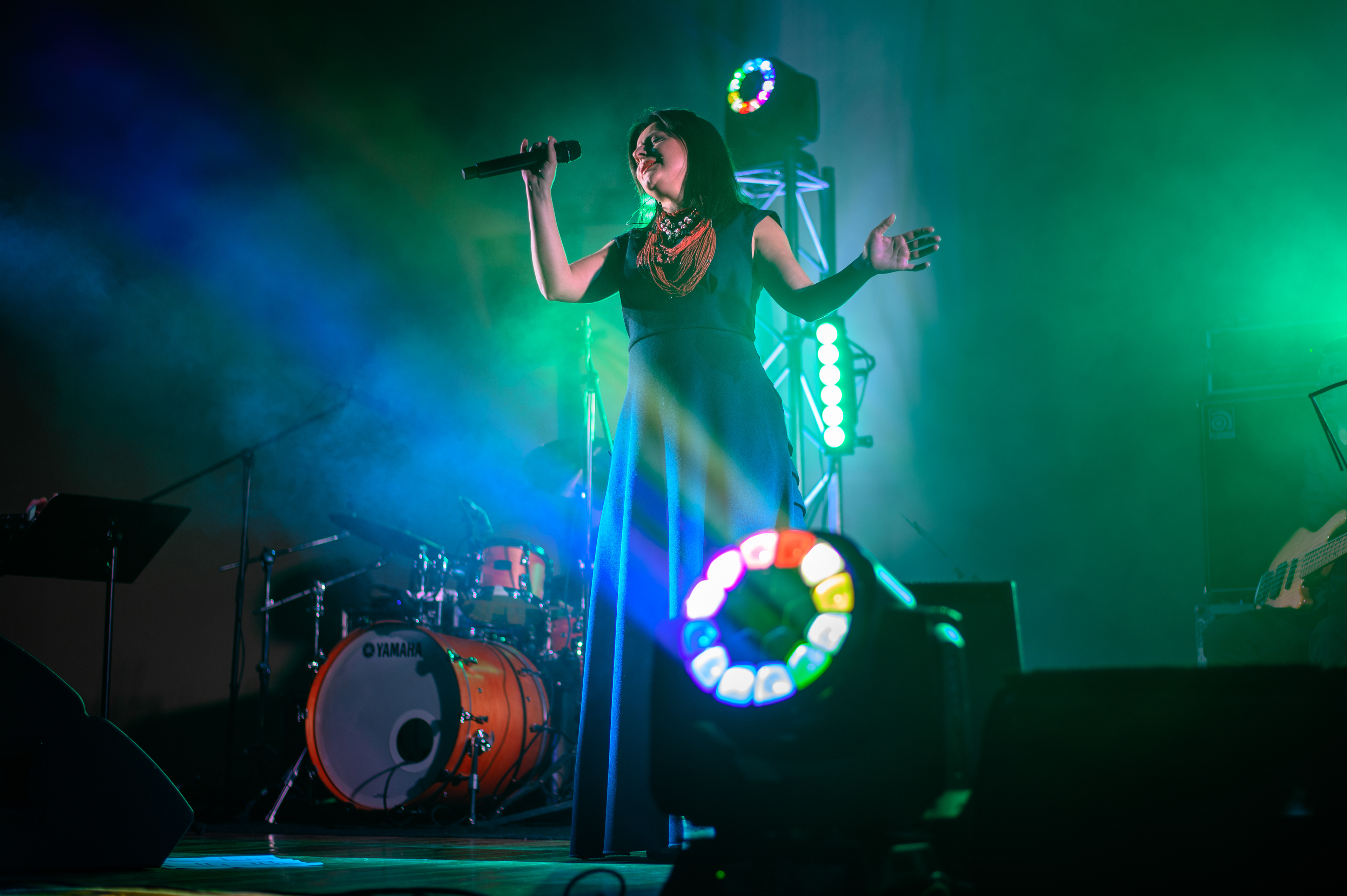 Singer Oksana Mukha performing with open arms in green and blue stage light