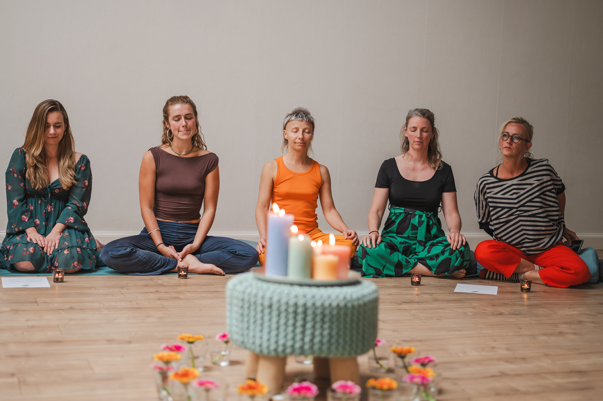Women meditating with closed eyes behind candles and flowers