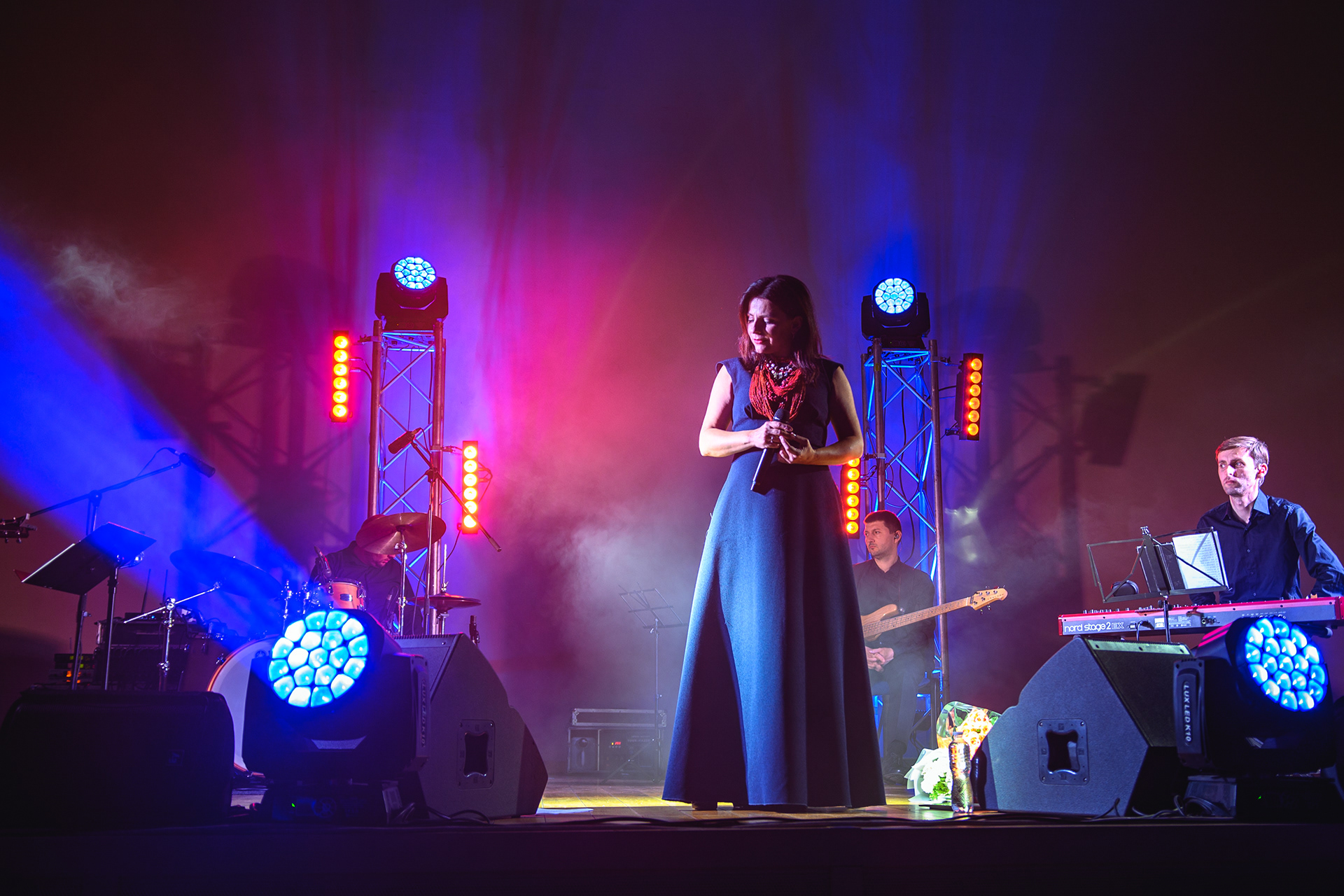 Oksana Mukha in a long blue dress on stage with her band under blue and red lights