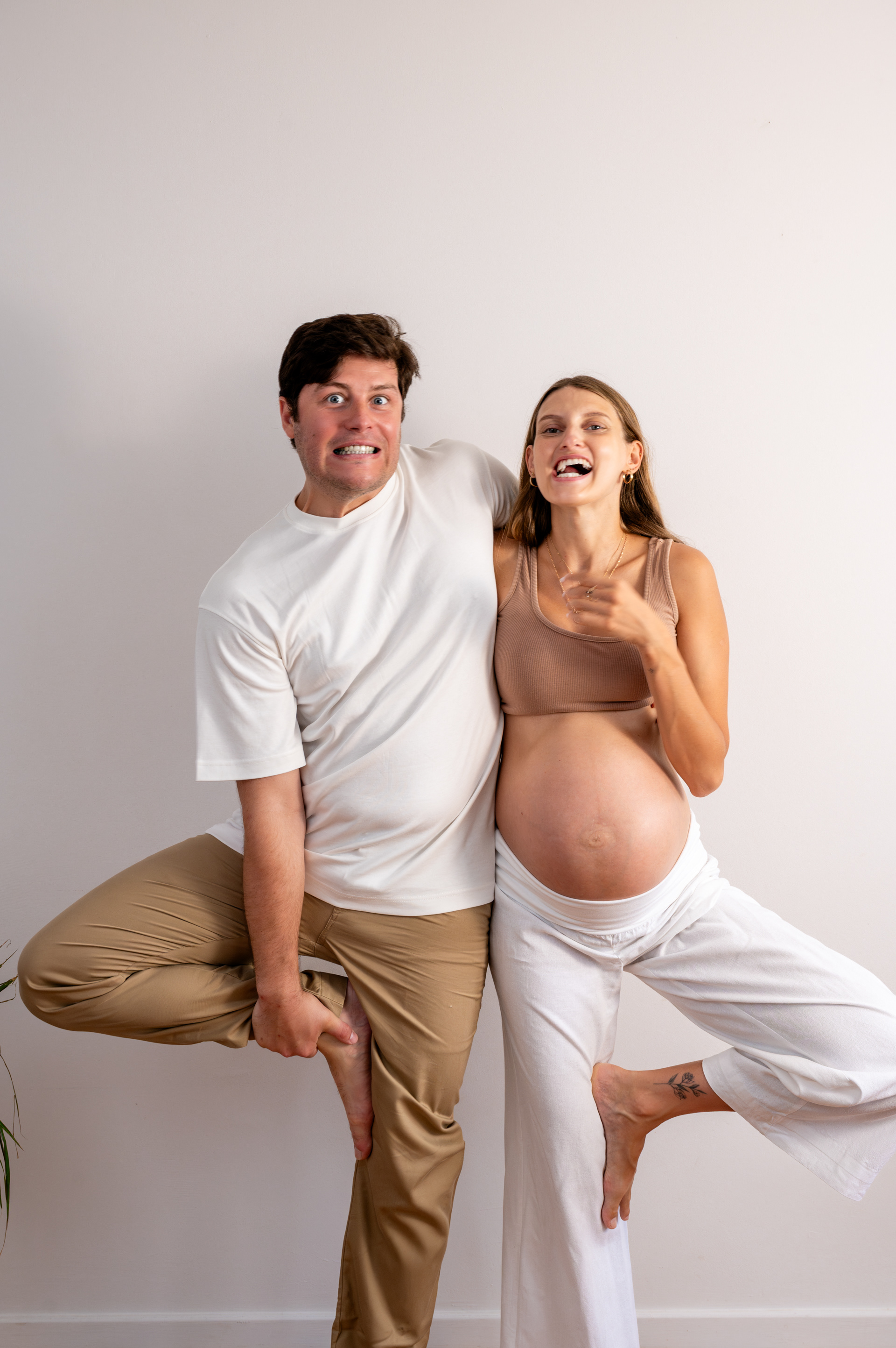 Pregnant yoga teacher and her partner in tree pose, playful maternity photo