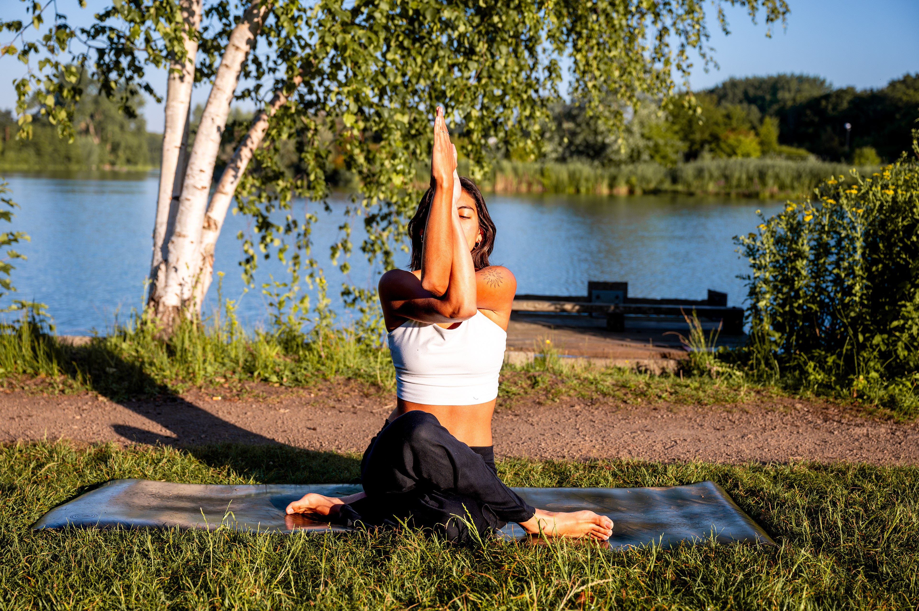 Eagle arms in a seated pose under birch trees by the water