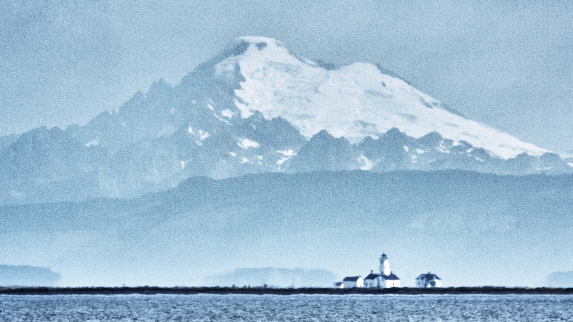 Mt Baker towers over Dungeness Lighthouse on a brilliant late summer day.The foreshortening power of a 400mm lens brings the mountain in on top of the lighthouse, more than 5 miles away at the end of the sand spit.