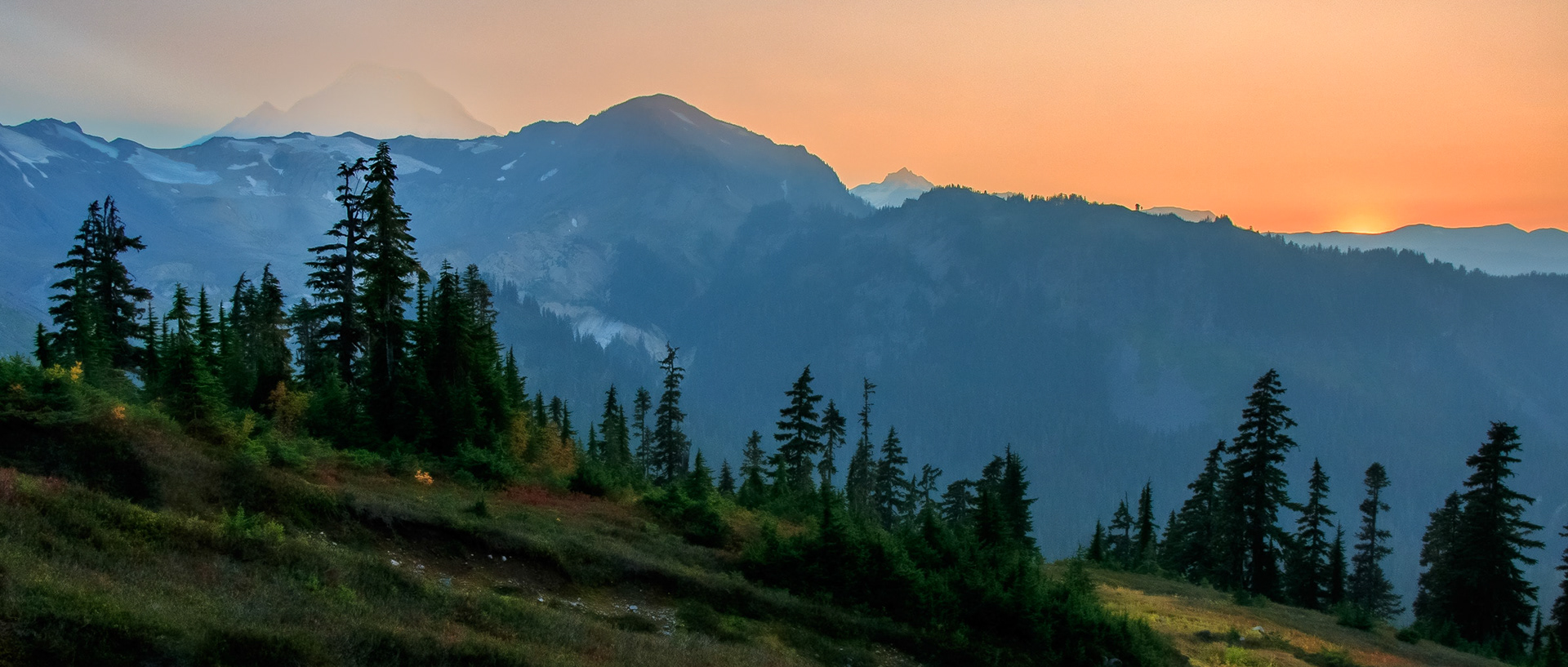 The setting sun paints a smoke filled sky a dusty red. Mt Baker is obscured inn smoke behind the local mountains