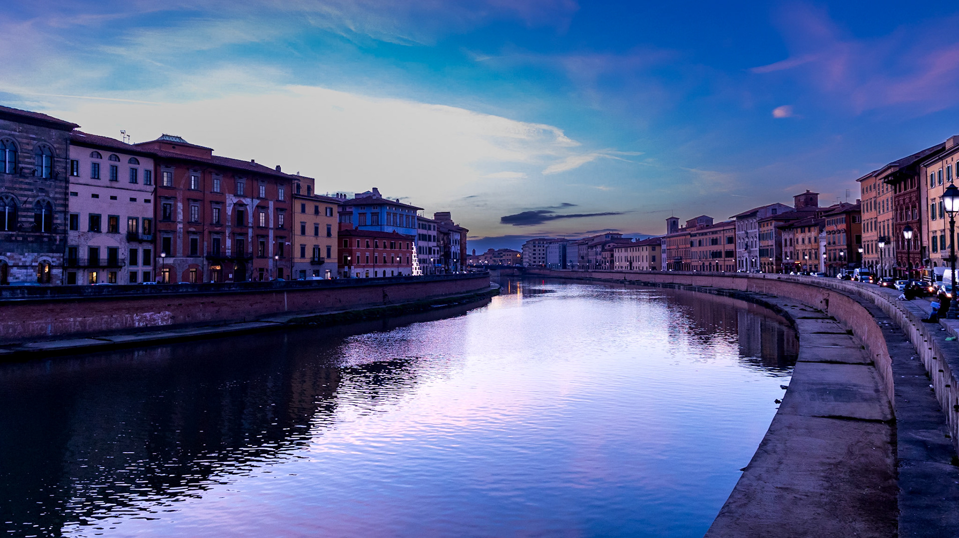Looking east along the River Arno as it curves through Pisa under the late evening sky