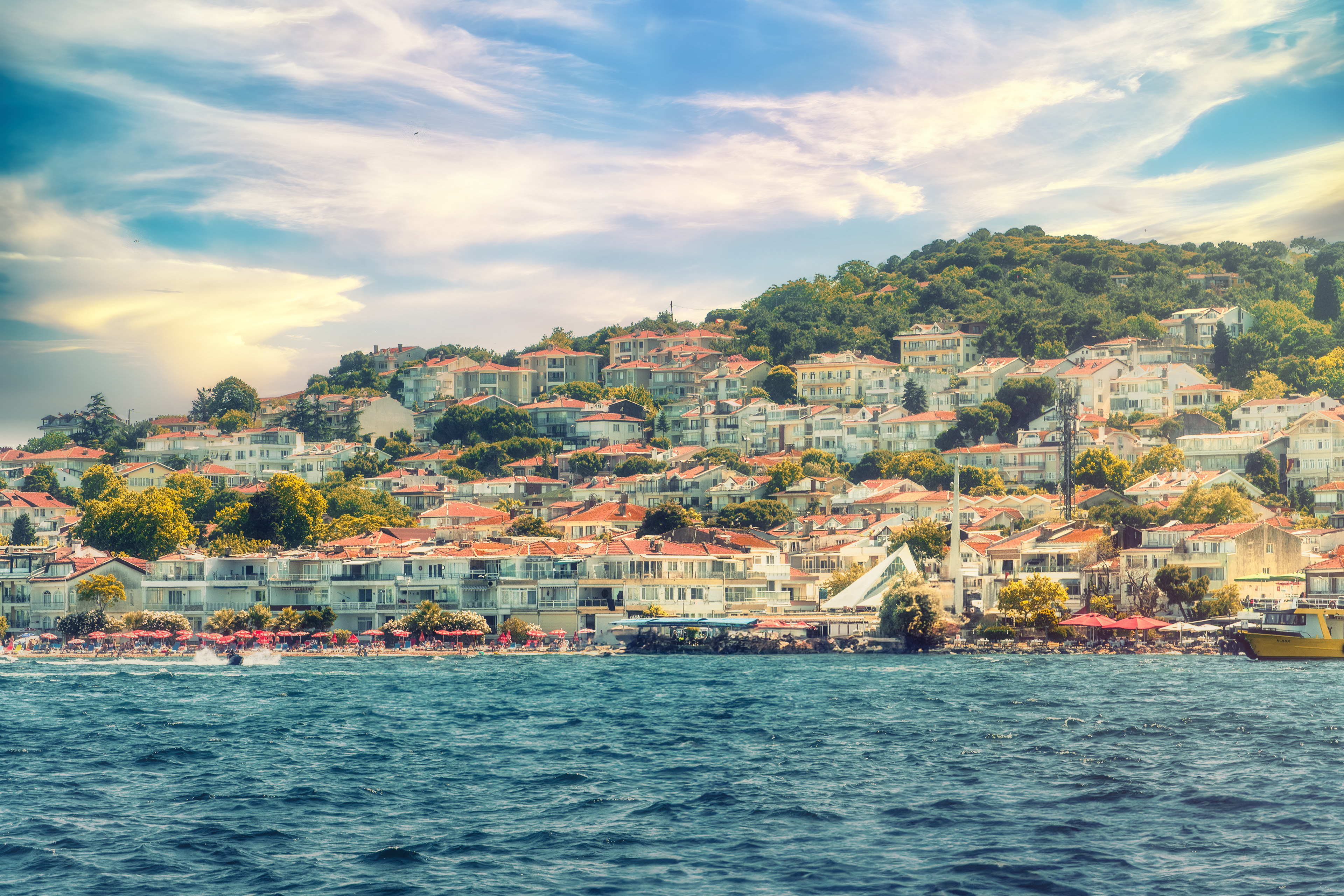 A peaceful town by the sea with red-roofed houses on a green hill. Calm, colorful, and full of summer light.