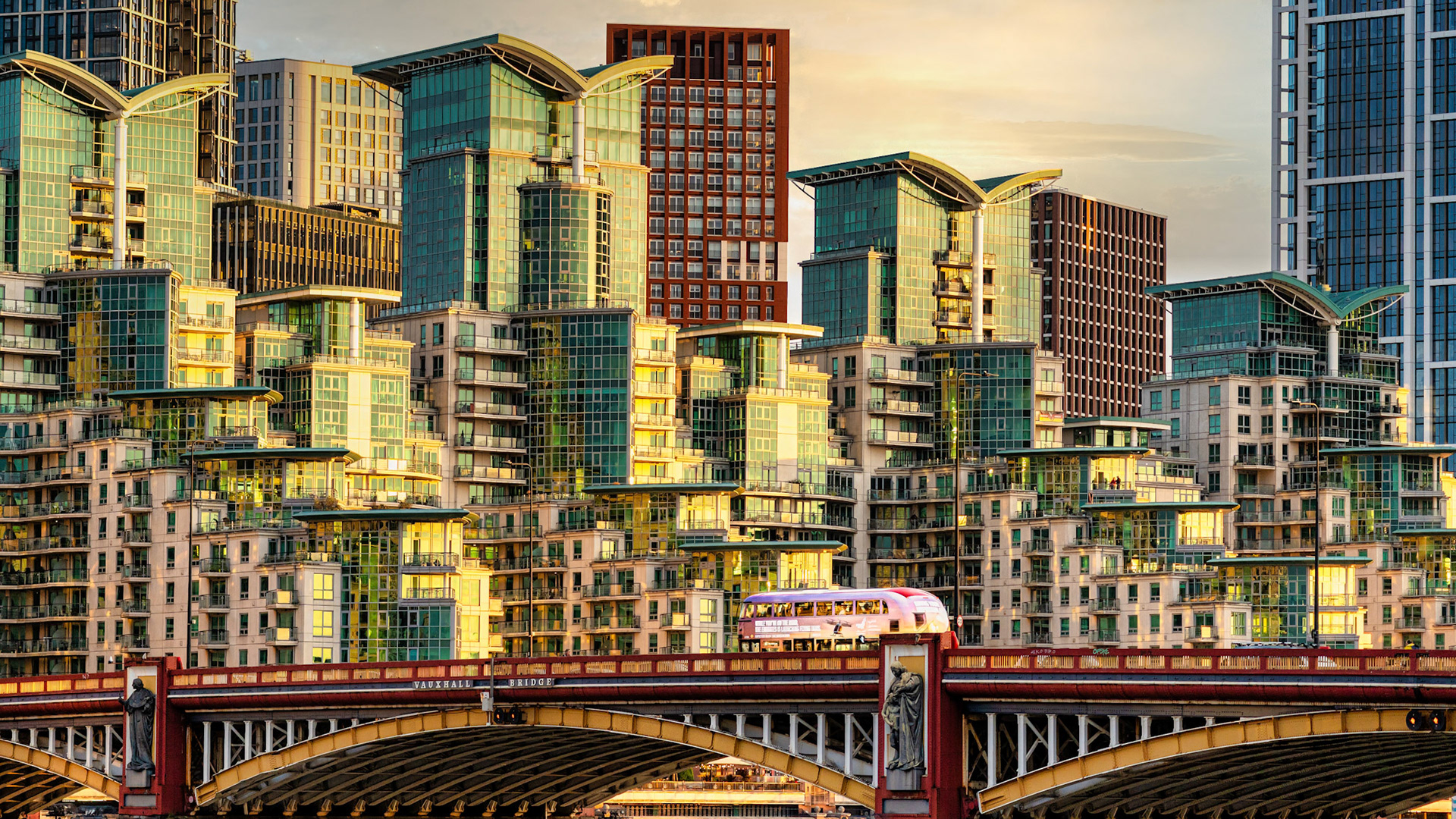 Golden hour reflections dance across the modern skyline of Vauxhall, as a classic London bus glides over the historic bridge below.