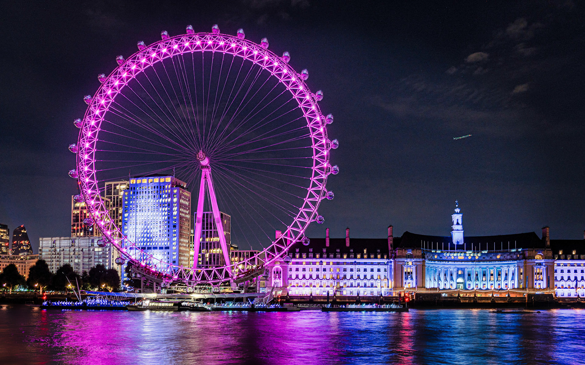 The London Eye radiates in vibrant pink, casting a luminous glow over the Thames and lighting up the heart of the city’s nightlife.