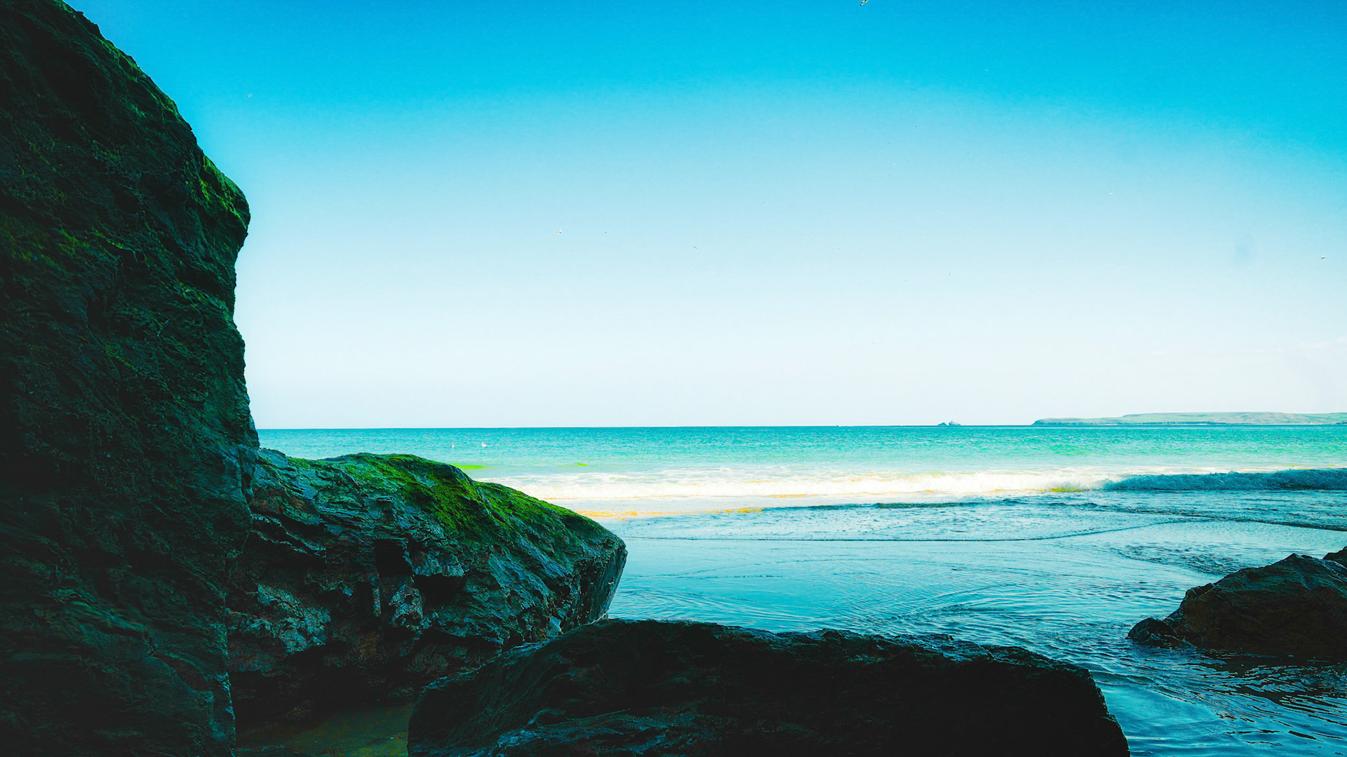 A quiet moment captured from within the shadows of coastal rocks, opening to a tranquil turquoise horizon where land and sky melt into one.