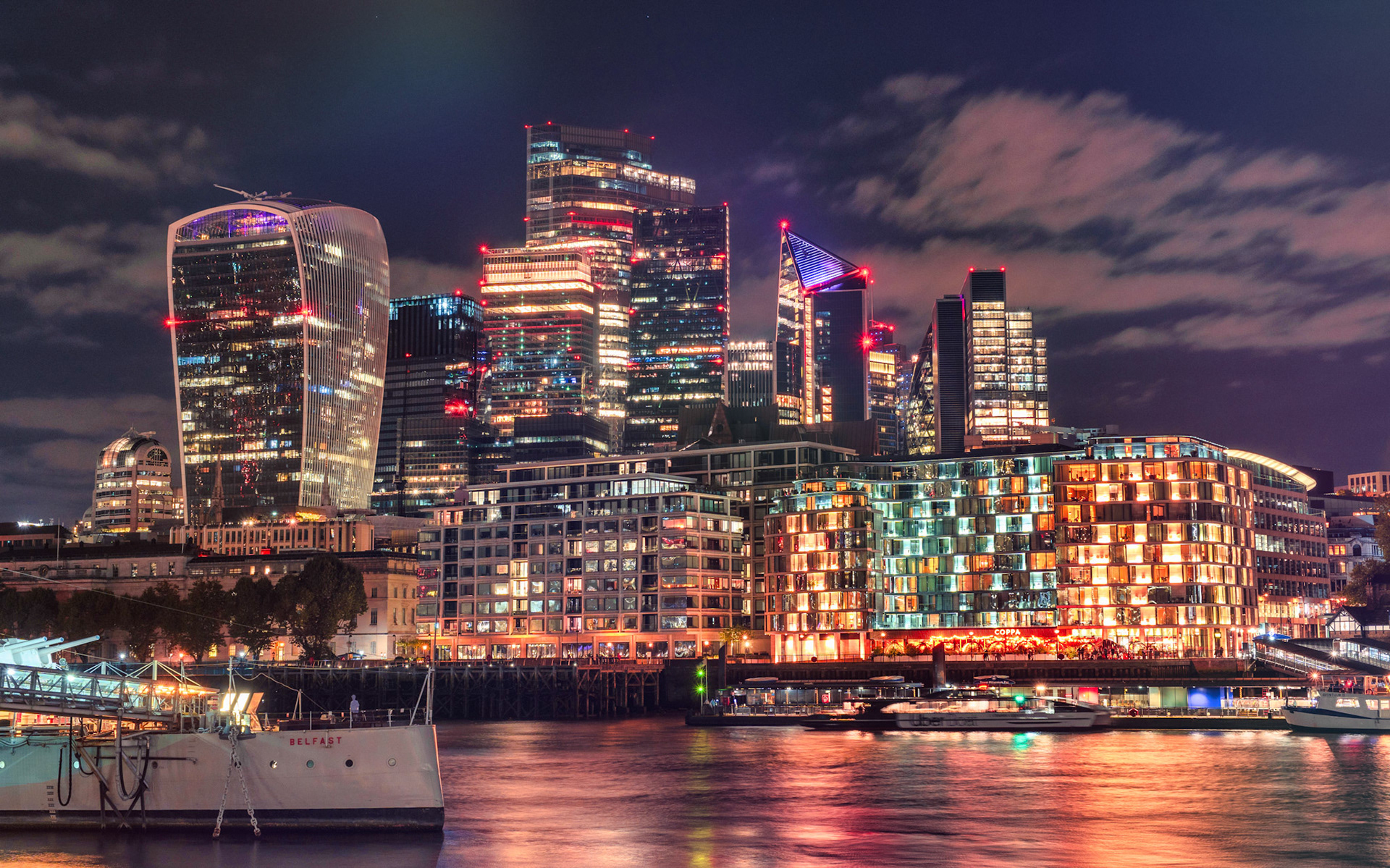 The vibrant lights of London’s financial district shimmer across the Thames, where modern architecture meets the pulse of the city’s nightlife.