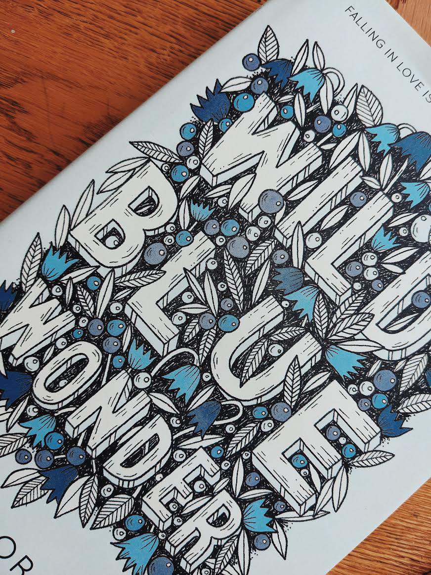 the image shows a pale blue book cover. the title reads "Wild Blue Wonder" in large letters. The type is surrounded by flowers, leaves and berries in various shades of blue. A close up