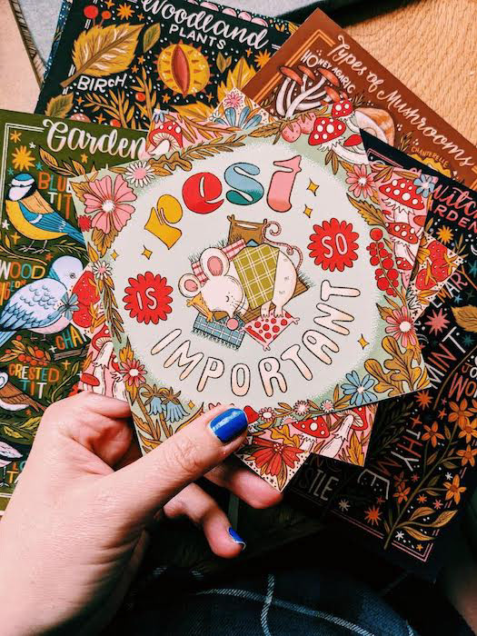 the image shows a close of of a colourful art print. the text reads "rest is so important" and shows a cute cartoon mouse having a nap underneath some cosy blankets