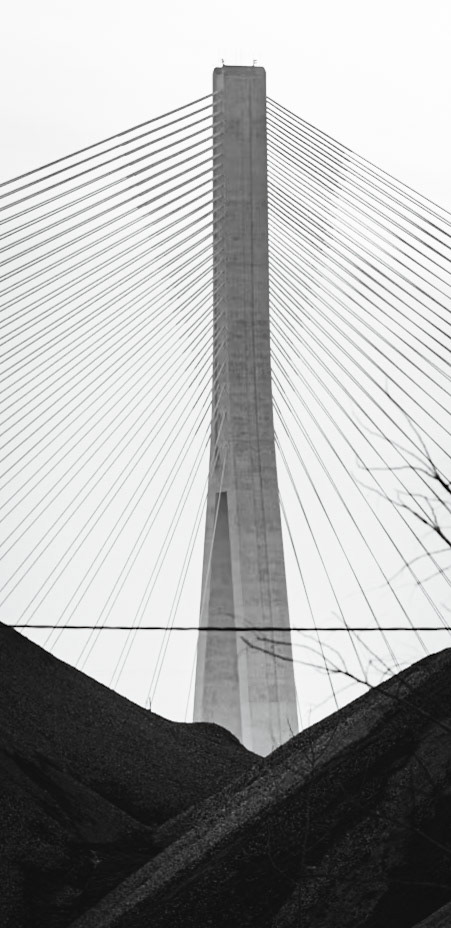 Monolithic Noir study of the Gordie Howe International Bridge, rendered with maximum depth of field to include foreground industrial grit. A.M. Stone | Archival Stone Photography