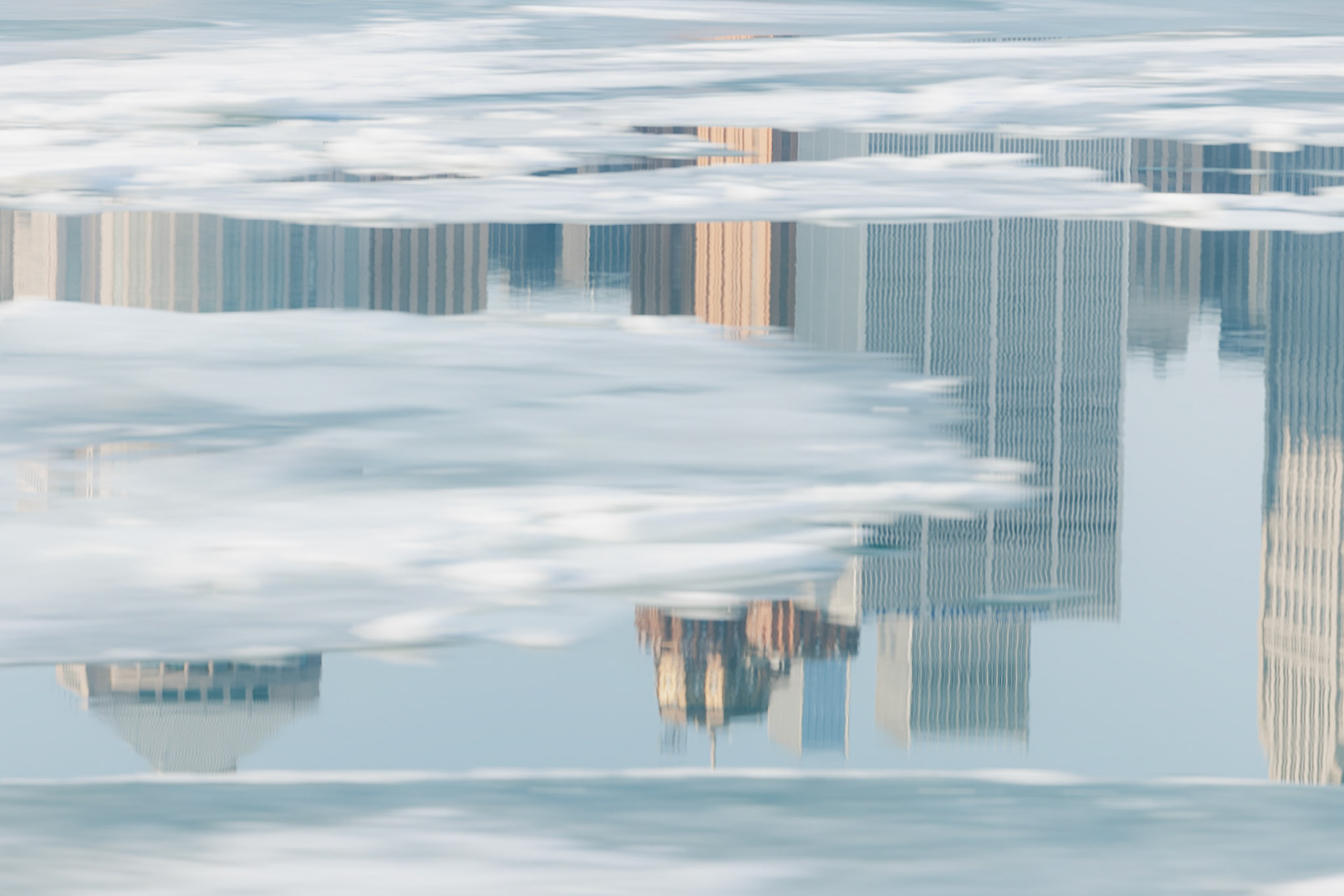 A whimsical reflection of the Detroit skyline in the turquoise Detroit River. Ice floes from the recent warm weather mask the reflection.