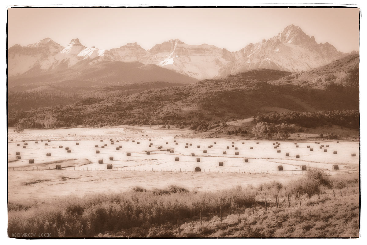 Hay rolls in morning frosty field with snow-capped peaks including Mount Sneffels in distance, Colorado