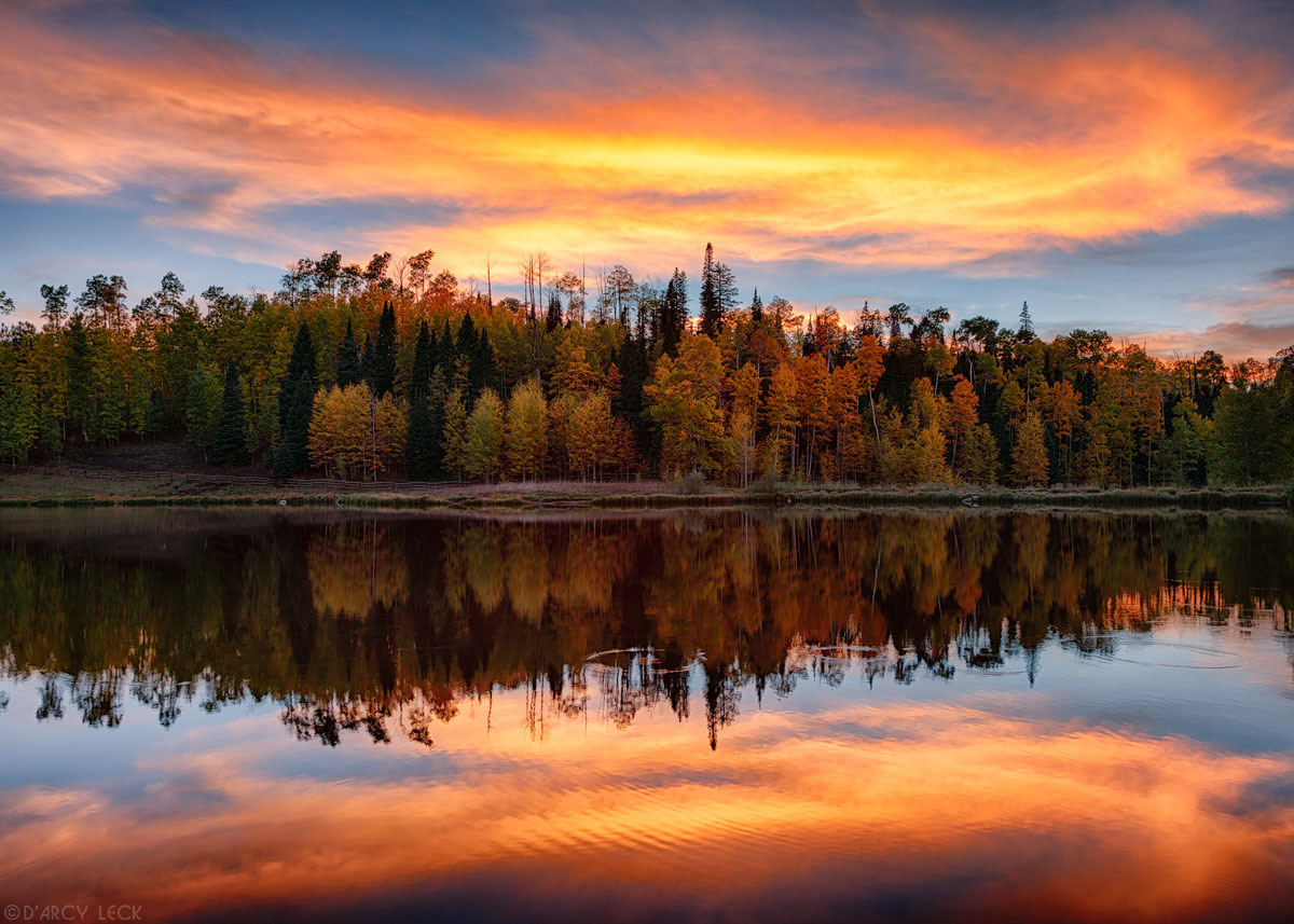 Sunset colored clouds and forest in Autumn colors reflects in Rowdy Lake at sunset, Colorado