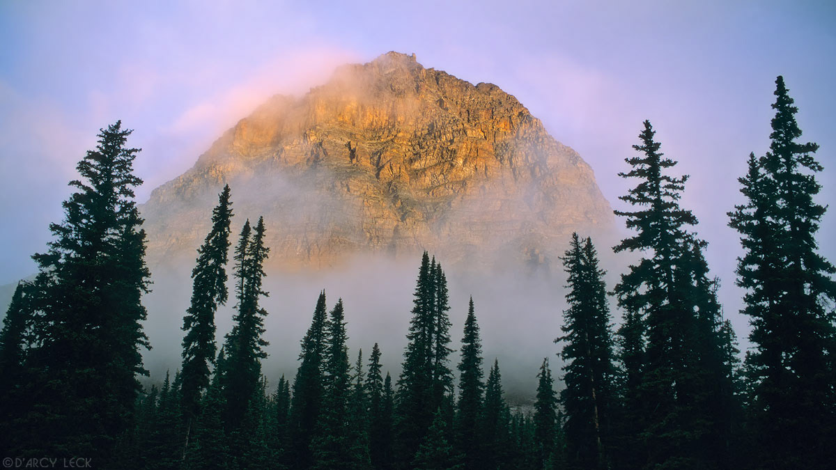 Clearing clouds allow first rays of sunrise to strike Pharaoh Peak in Banff National Park, Canada