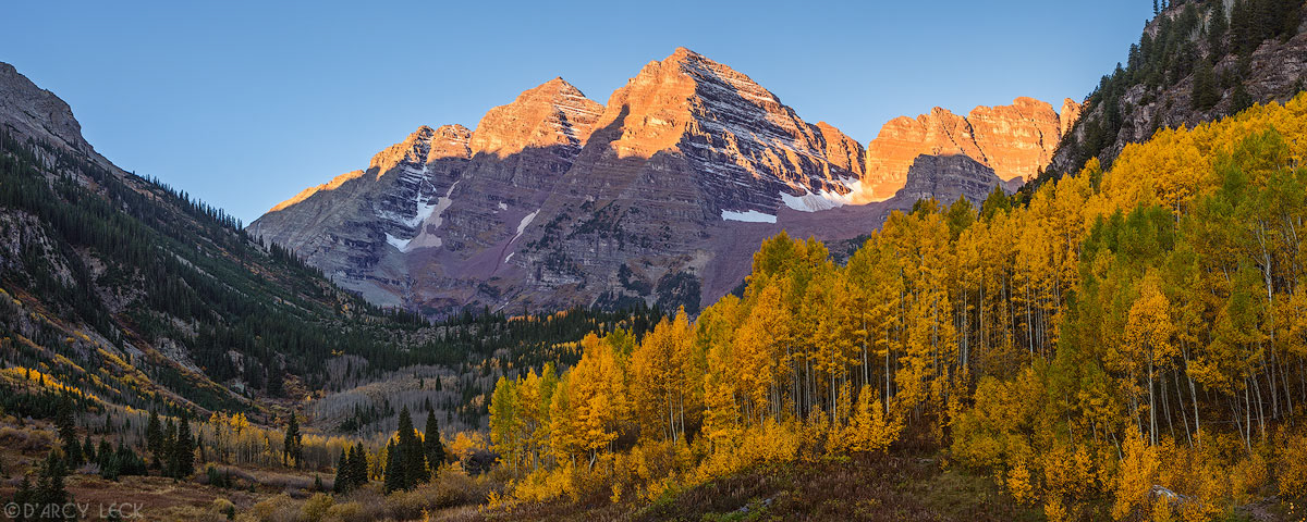 Morning sunlight illuminates the peaks of the Maroon Bells with aspen trees in autumn colors in the foreground, Colorado