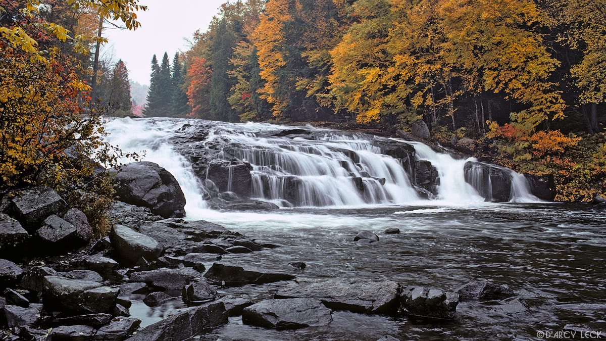 Buttermilk Falls of the Raquette River cascades over rocks through forest turning autumn colors, Adirondack Park, New York