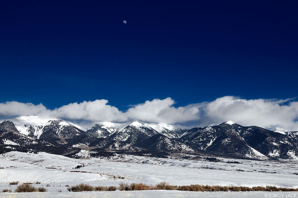 Winter storm clouds clear from Sangre de Cristo Mountains with a near full moon above in sky, San Luis Valley, Colorado