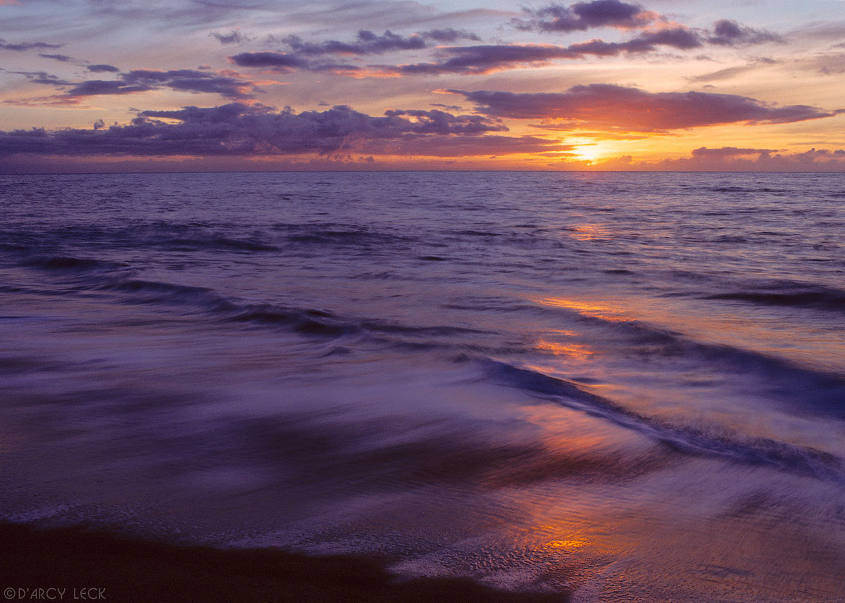 Sun sets in Pacific Ocean as surf rolls up beach, Polihale State Park, Kauai, Hawaii