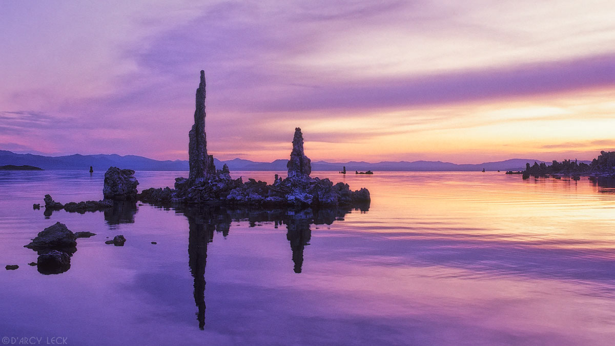 Tufa formations are silhouetted against a dawn sky and reflected in Mono Lake, California