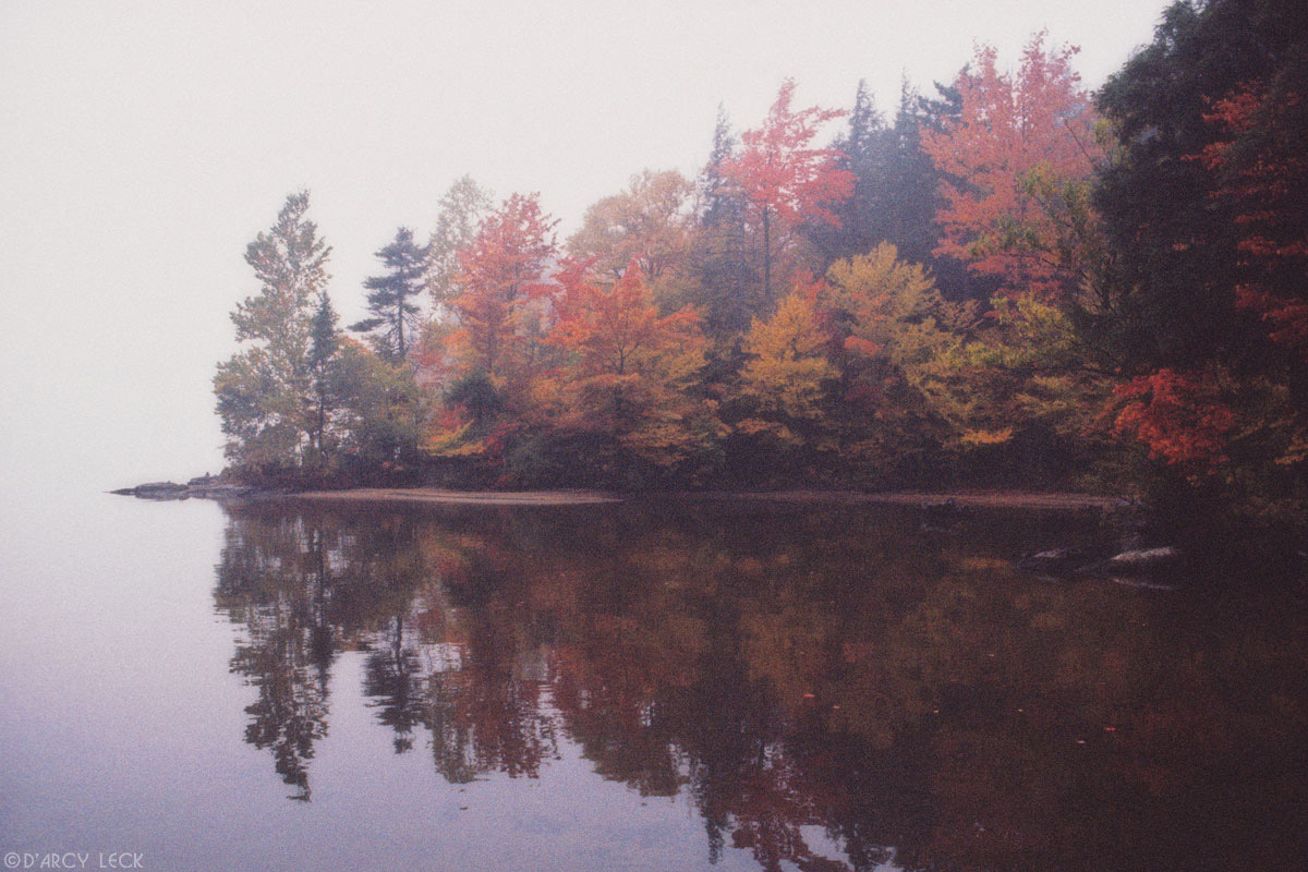 Peninsula with autumn trees extends out into foggy Blue Mountain Lake, Adirondack Park, New York
